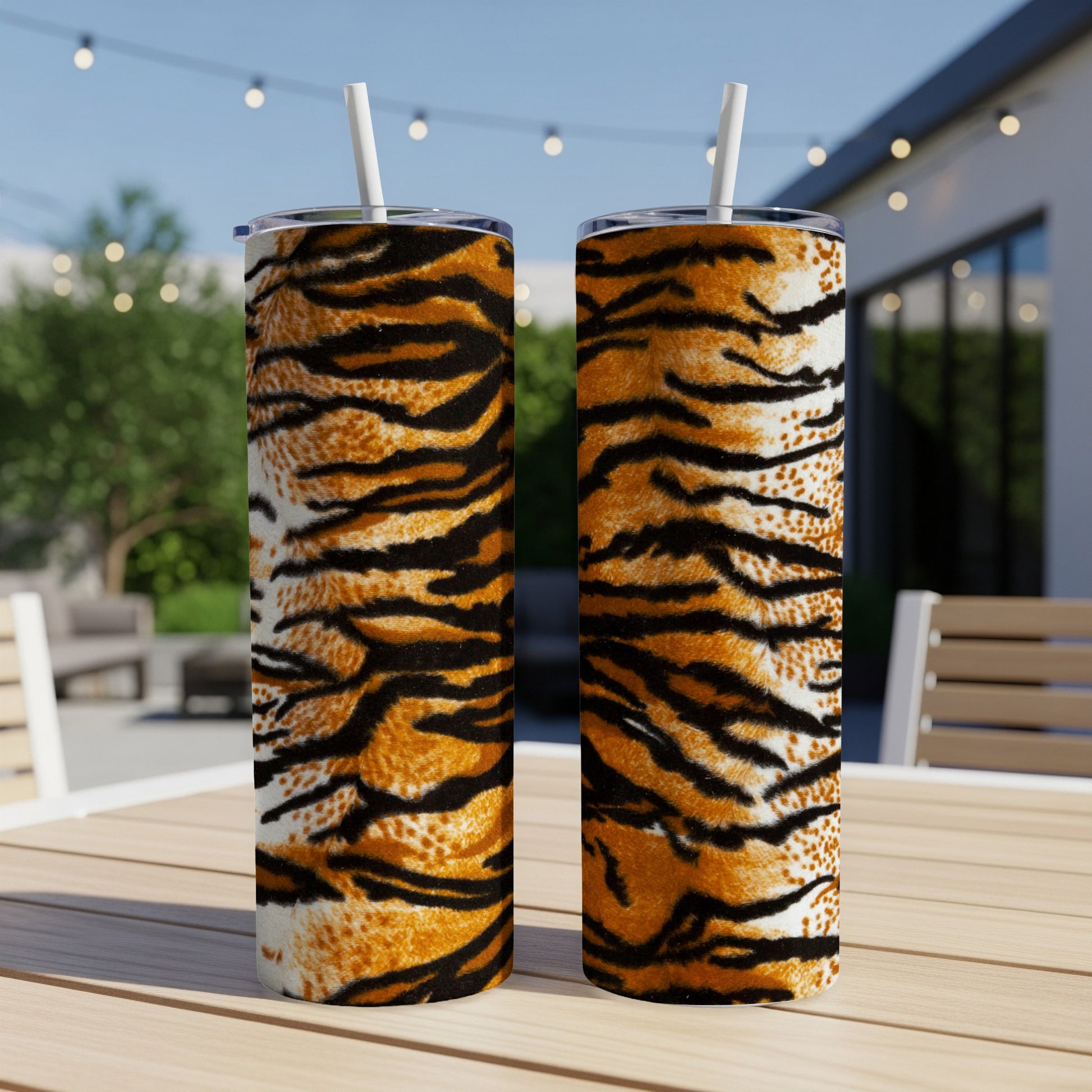 Two tumblers with tiger stripe patterns and white straws on a wooden table.