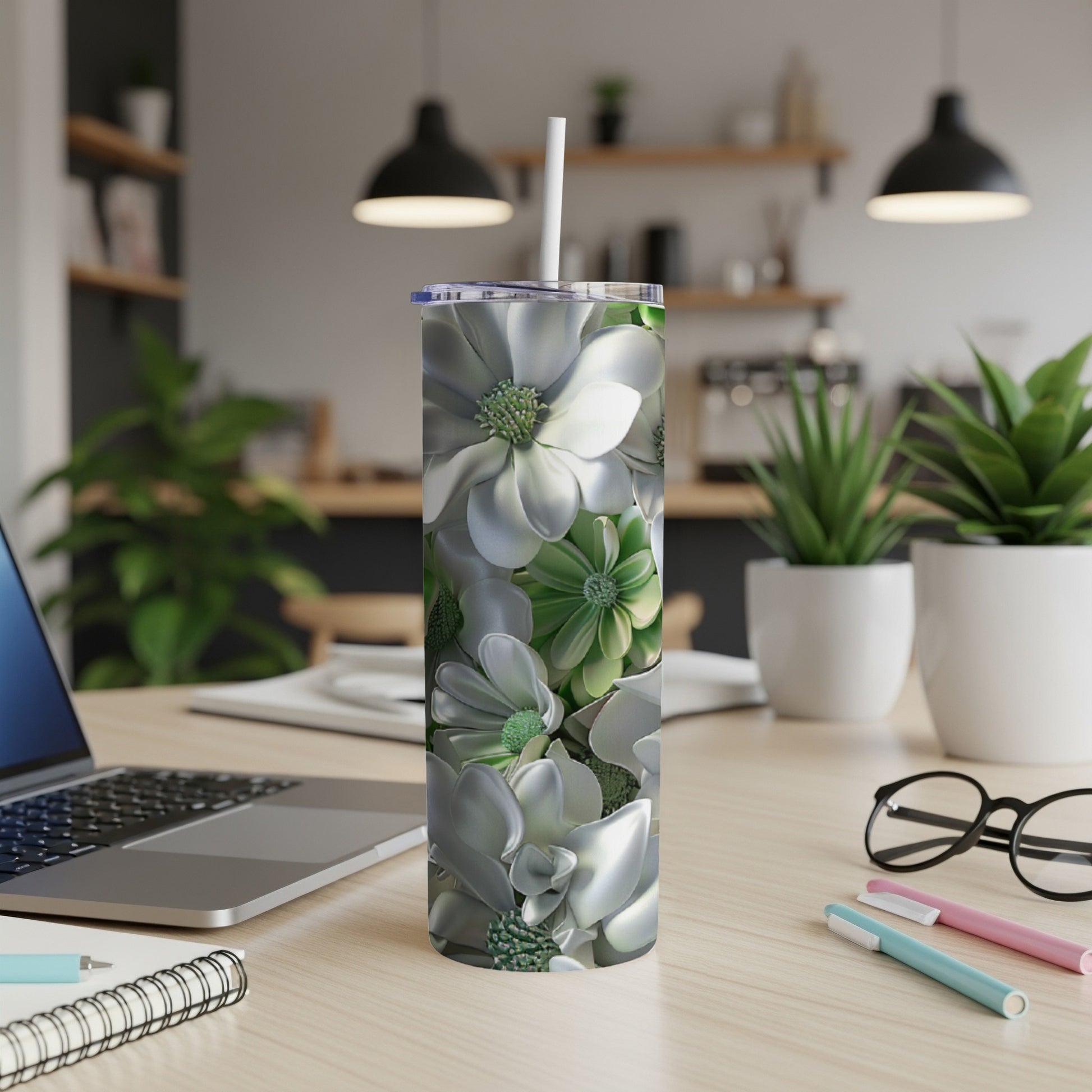 Silver floral tumbler with a straw on a desk next to a laptop.