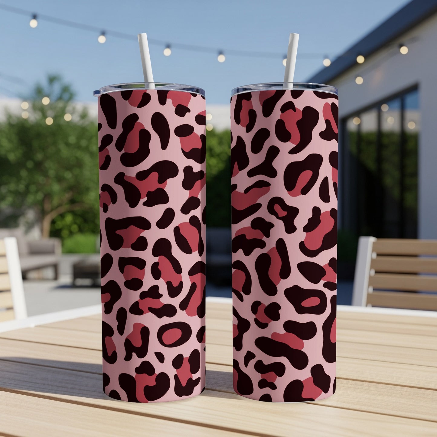 Two pink tumblers with leopard print and white straws on a wooden table.