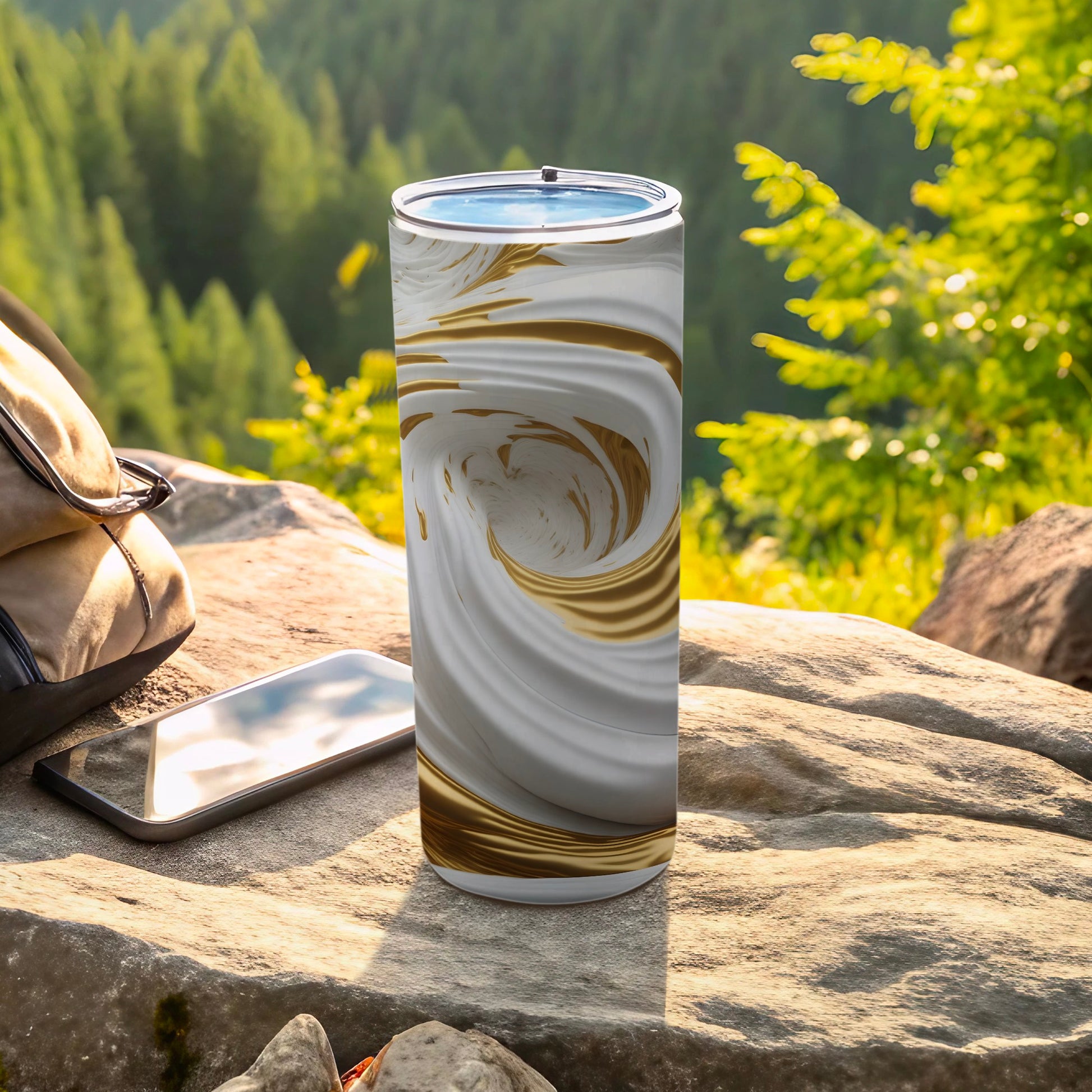White and gold marbled tumbler on rock next to phone and backpack.