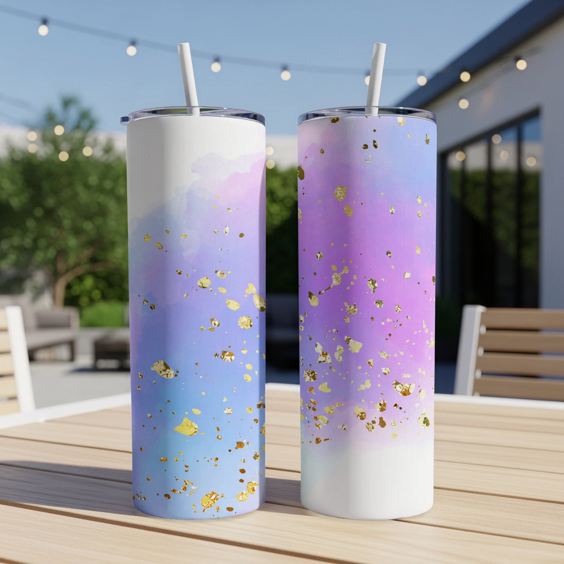 Two tumblers with watercolor and gold glitter designs on a patio table.
