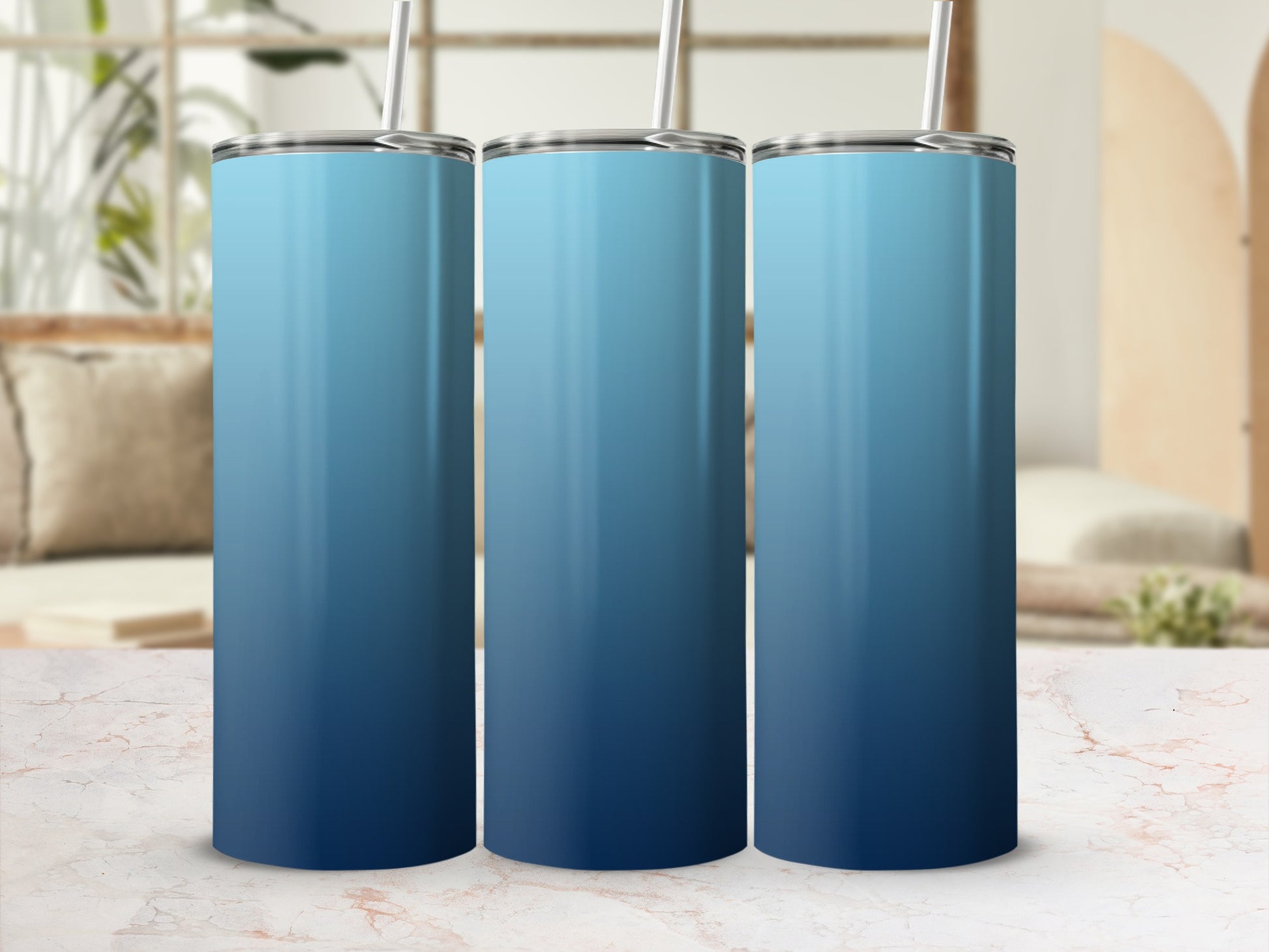 Three blue gradient tumblers with straws on a marble surface.