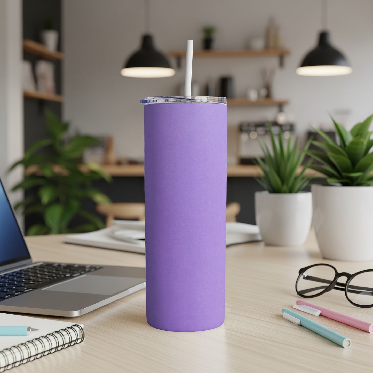 Purple tumbler with straw on a desk with a laptop and plants.