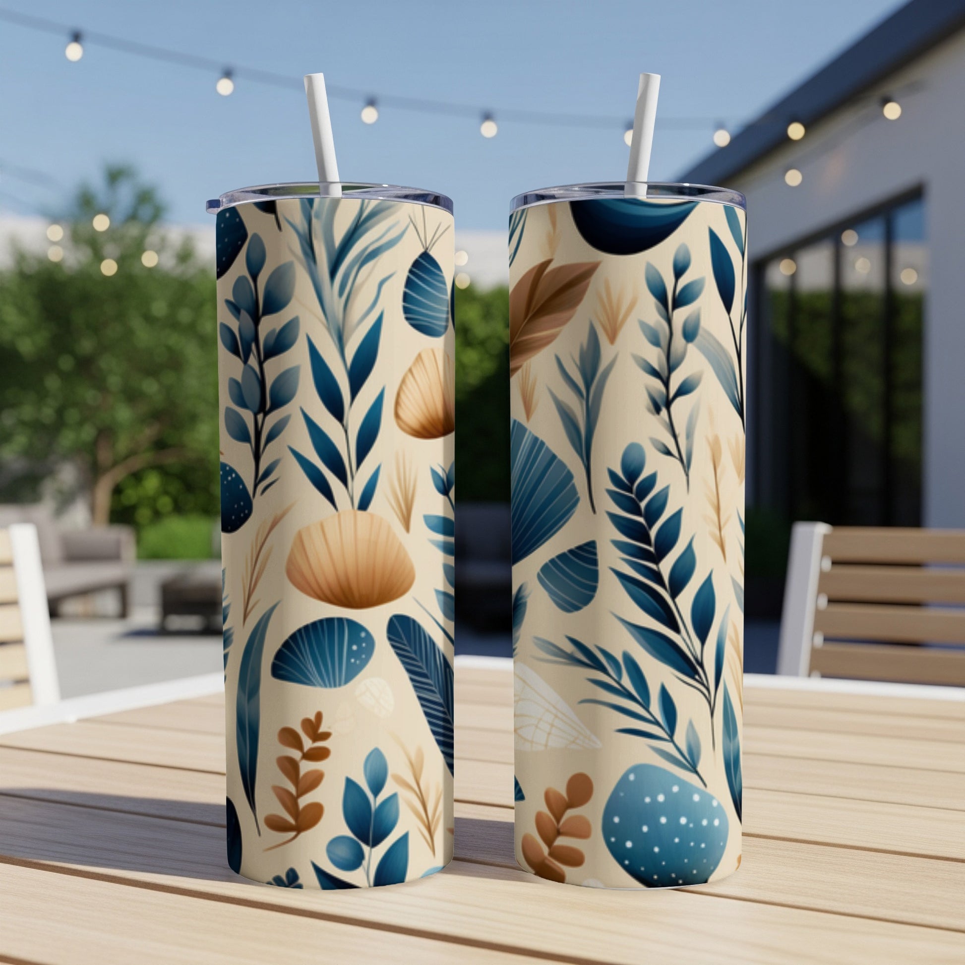 Two tumblers with botanical pattern of leaves and shells on a table outdoors.