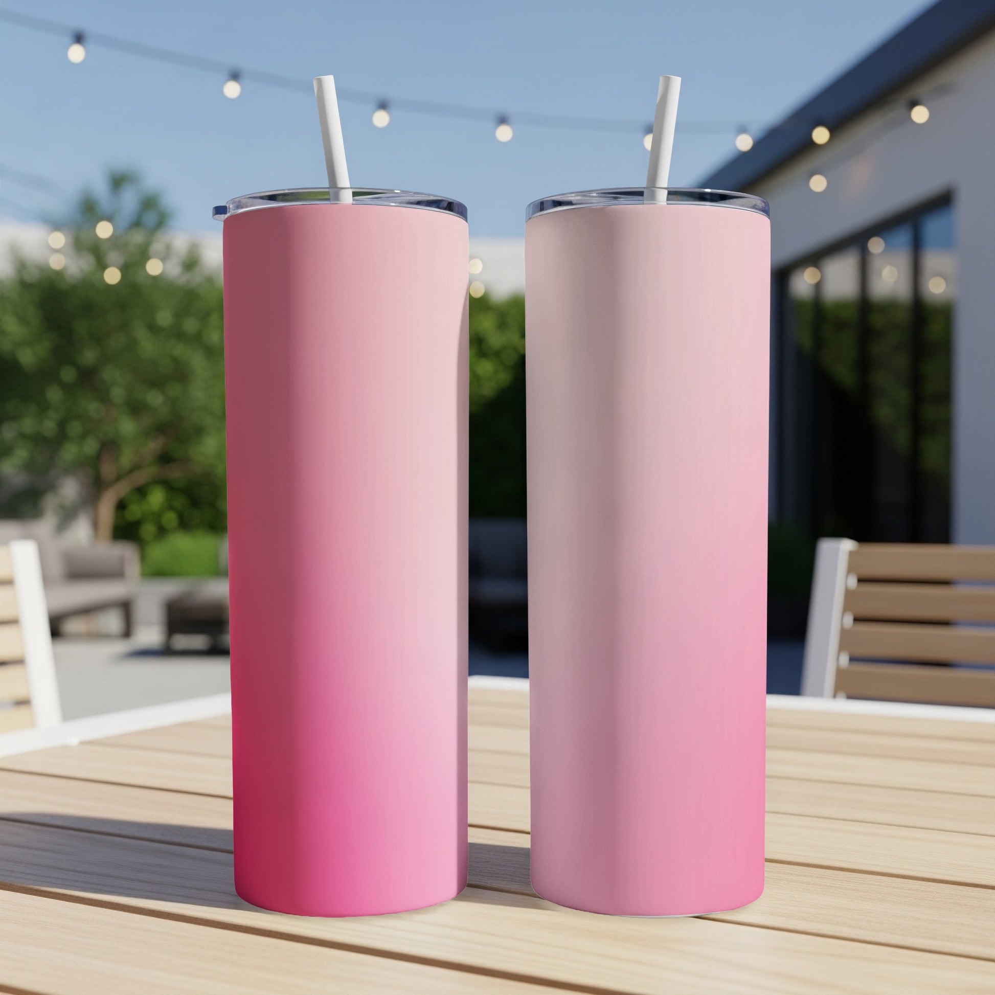 Two pink gradient tumblers with straws sit on a wooden table outdoors.