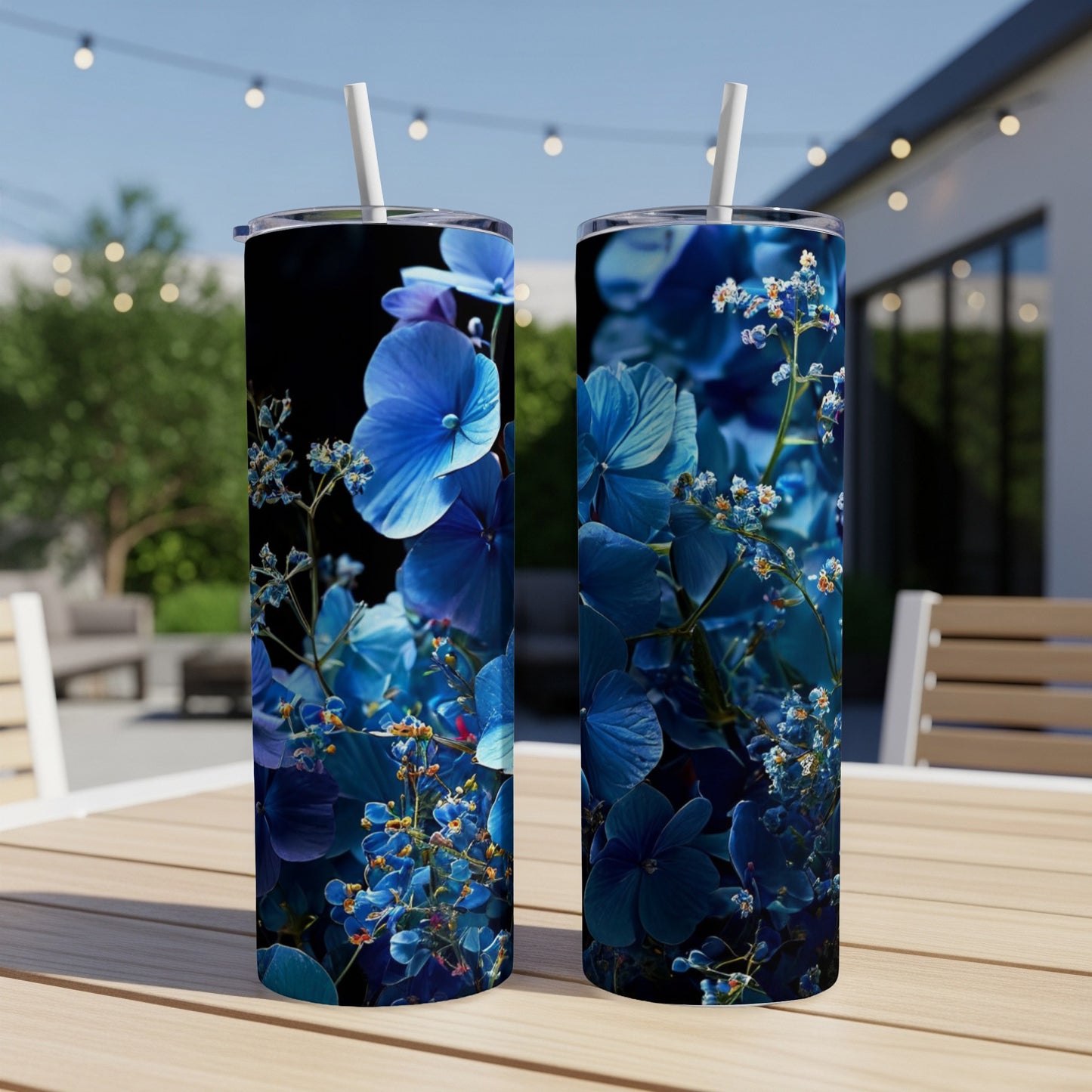Two blue hydrangea tumblers with straws on a table outdoors.
