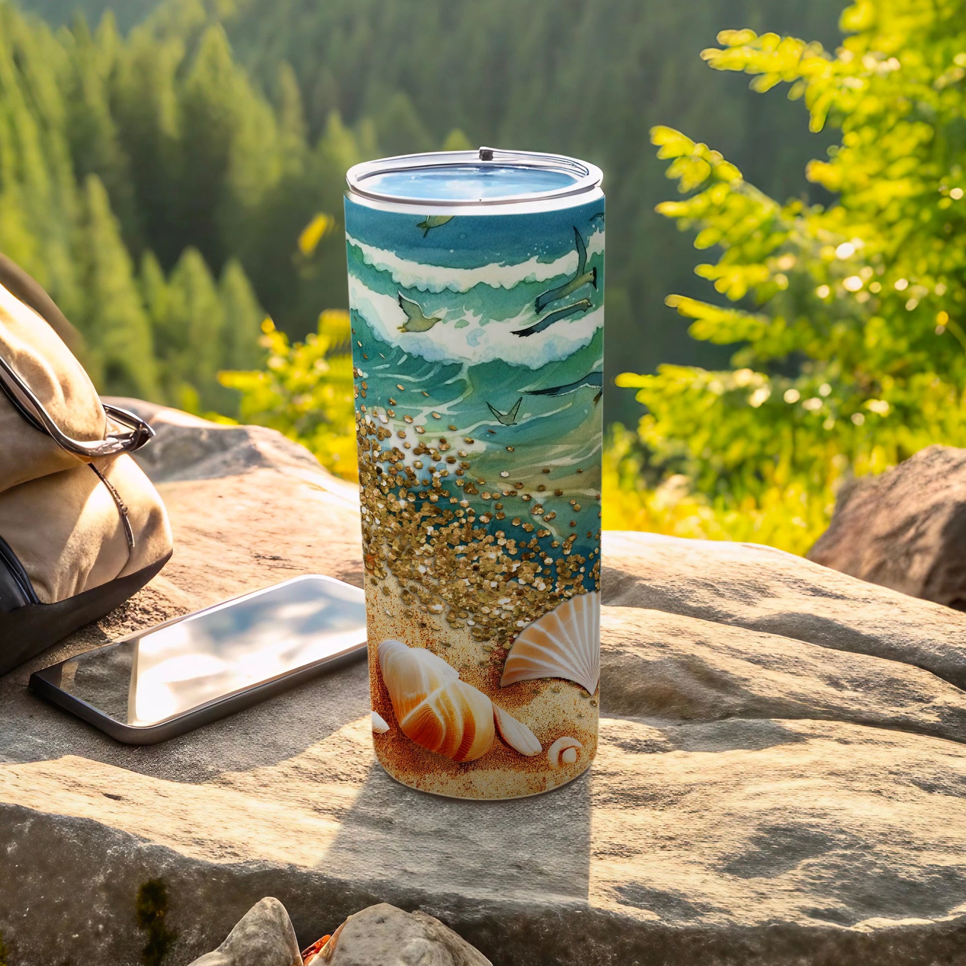 Seashell and wave patterned tumbler with sparkling glitter, resting on rocks.