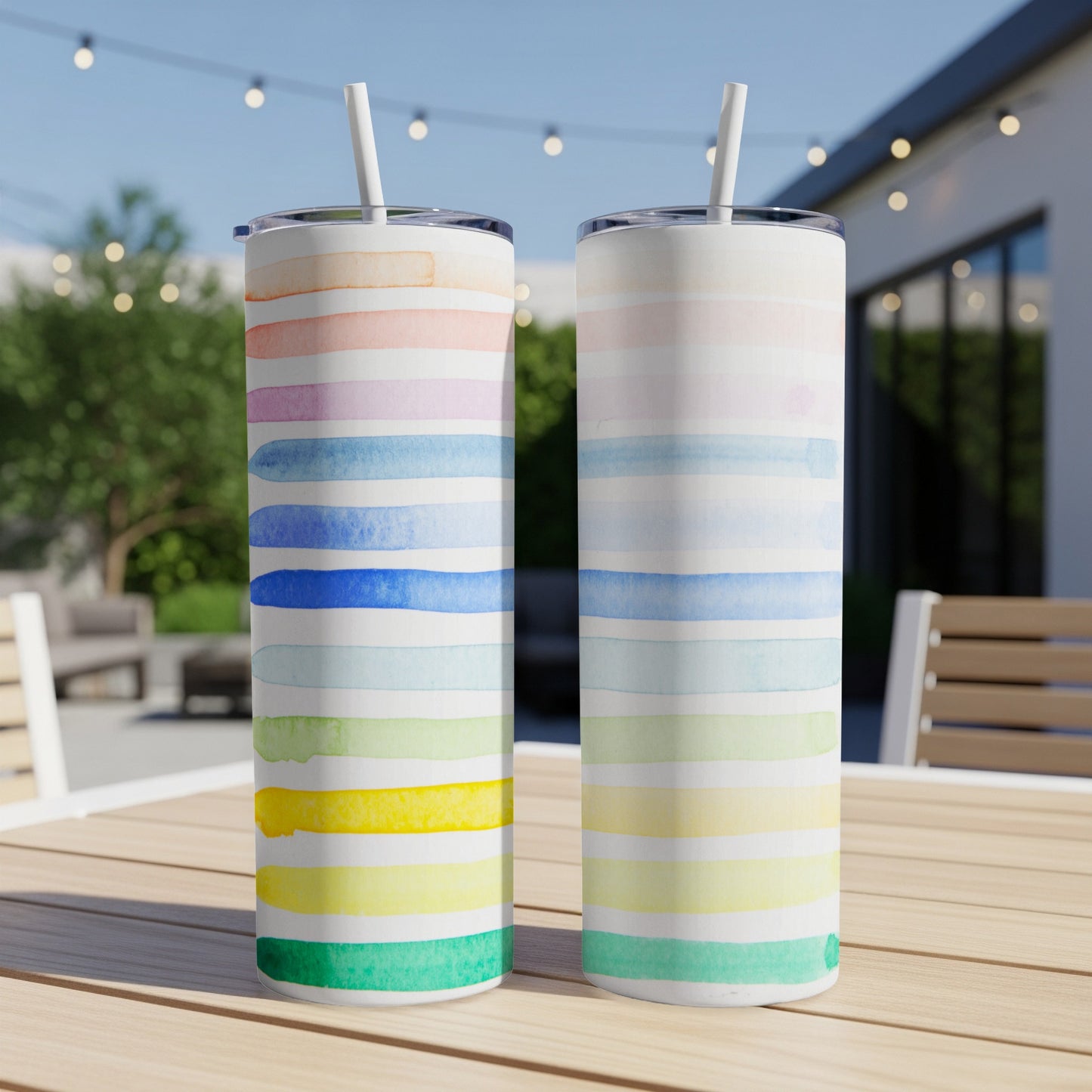 Two tumblers with pastel watercolor stripes on a wooden table outdoors.