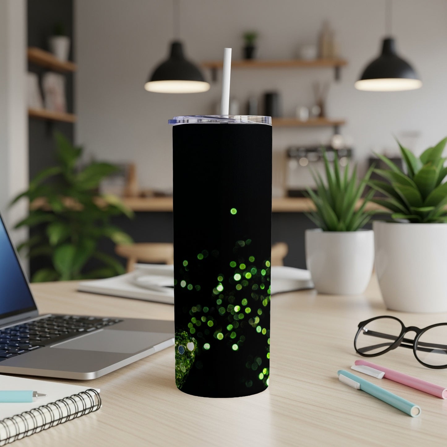 Black tumbler with green glitter design, straw, on a desk.