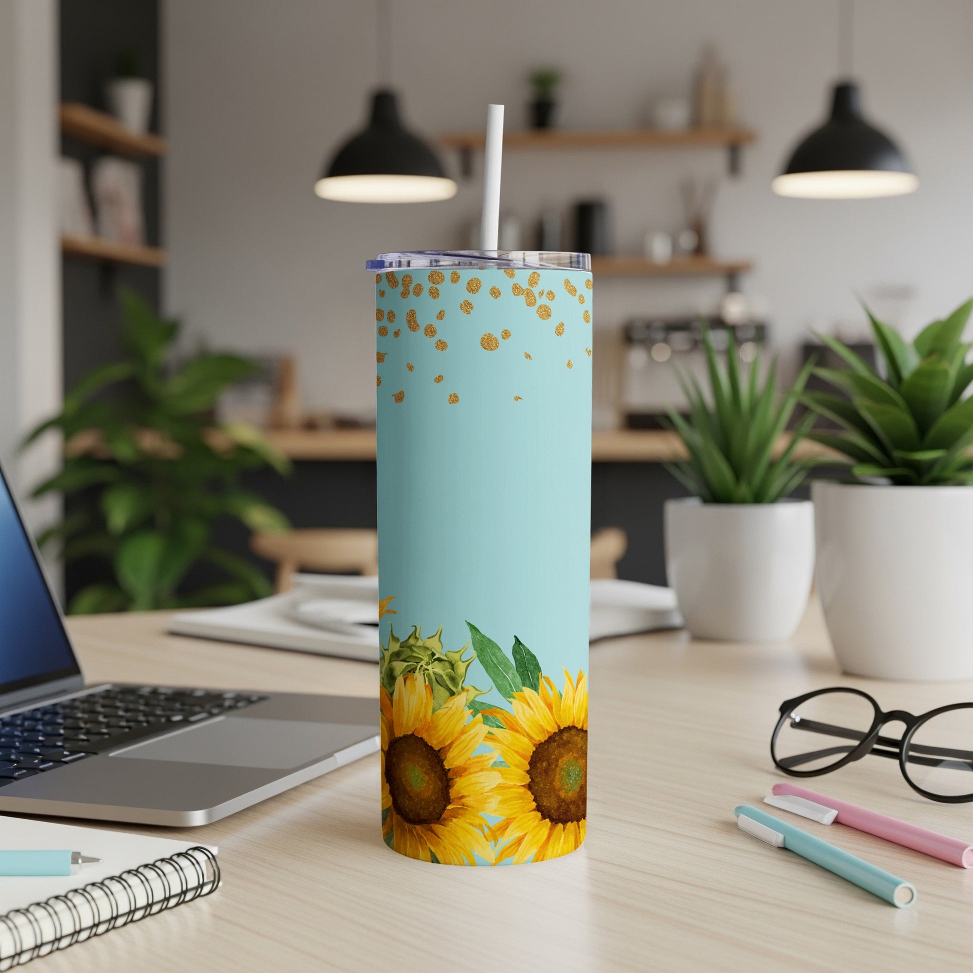 Blue tumbler with sunflowers and gold glitter, resting on a desk.