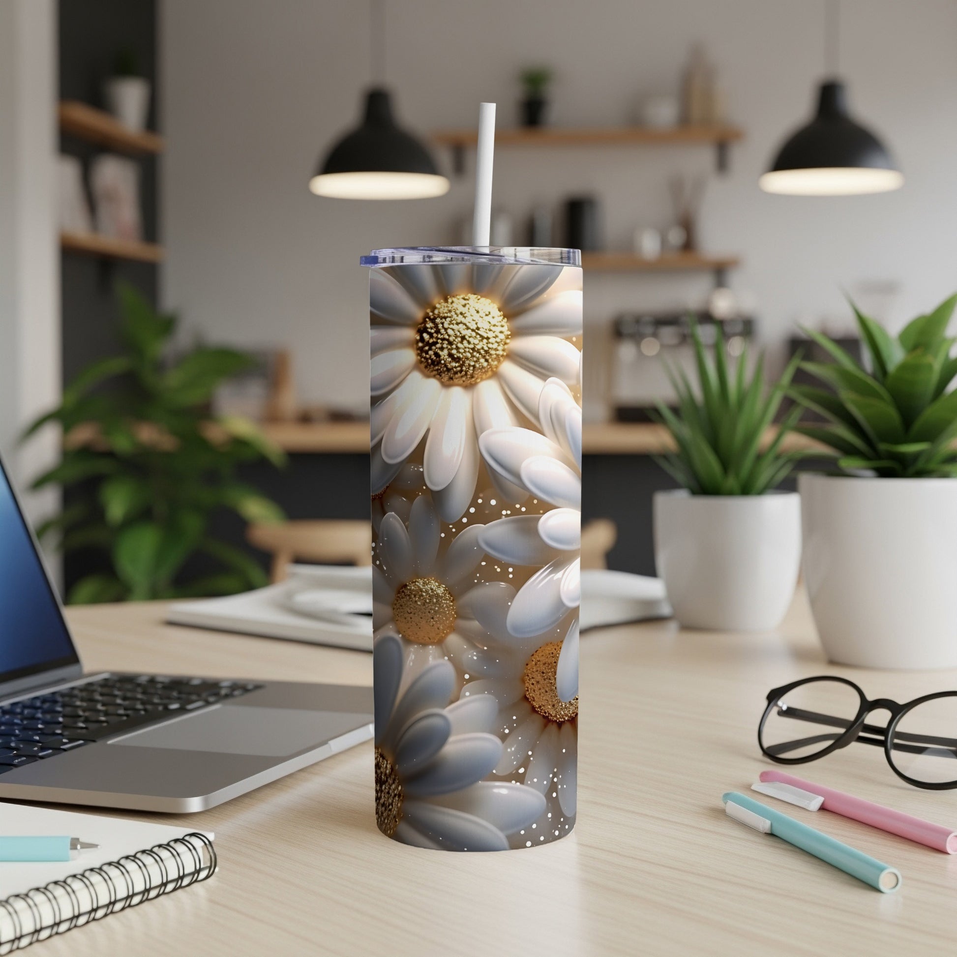 White daisy flowers on a tall tumbler with a straw on a desk.
