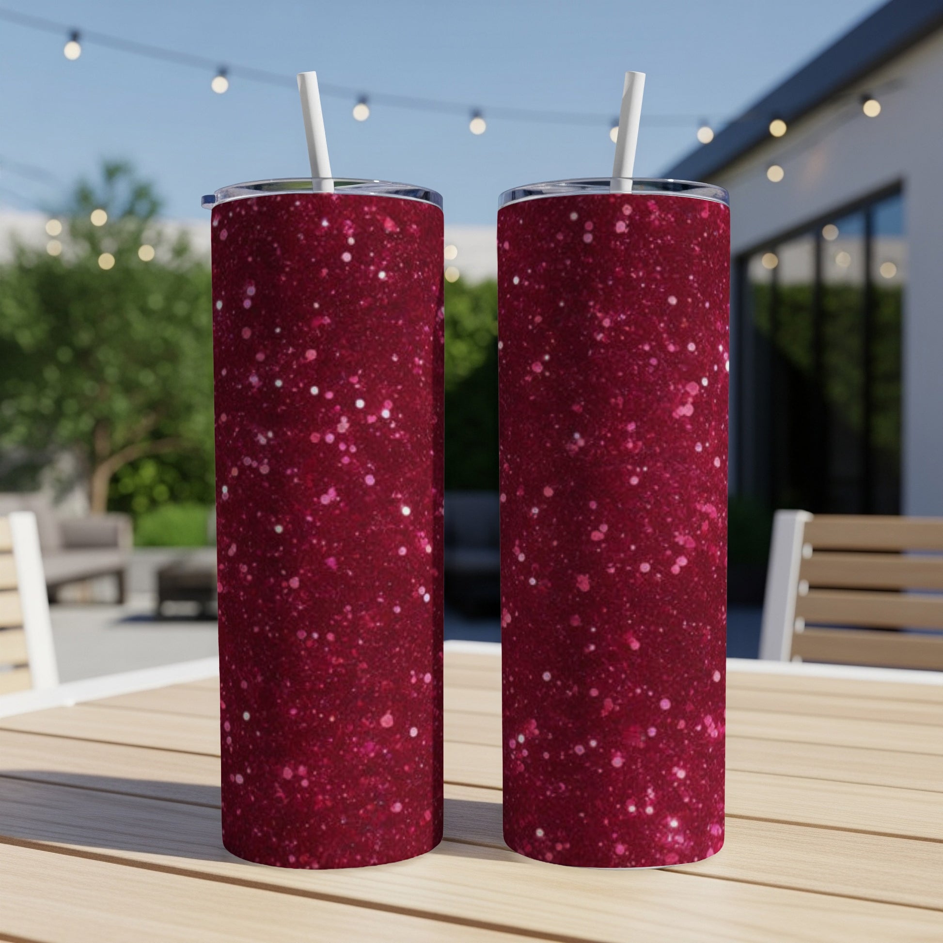 Two dark pink glitter tumblers with straws on a wooden table outdoors.