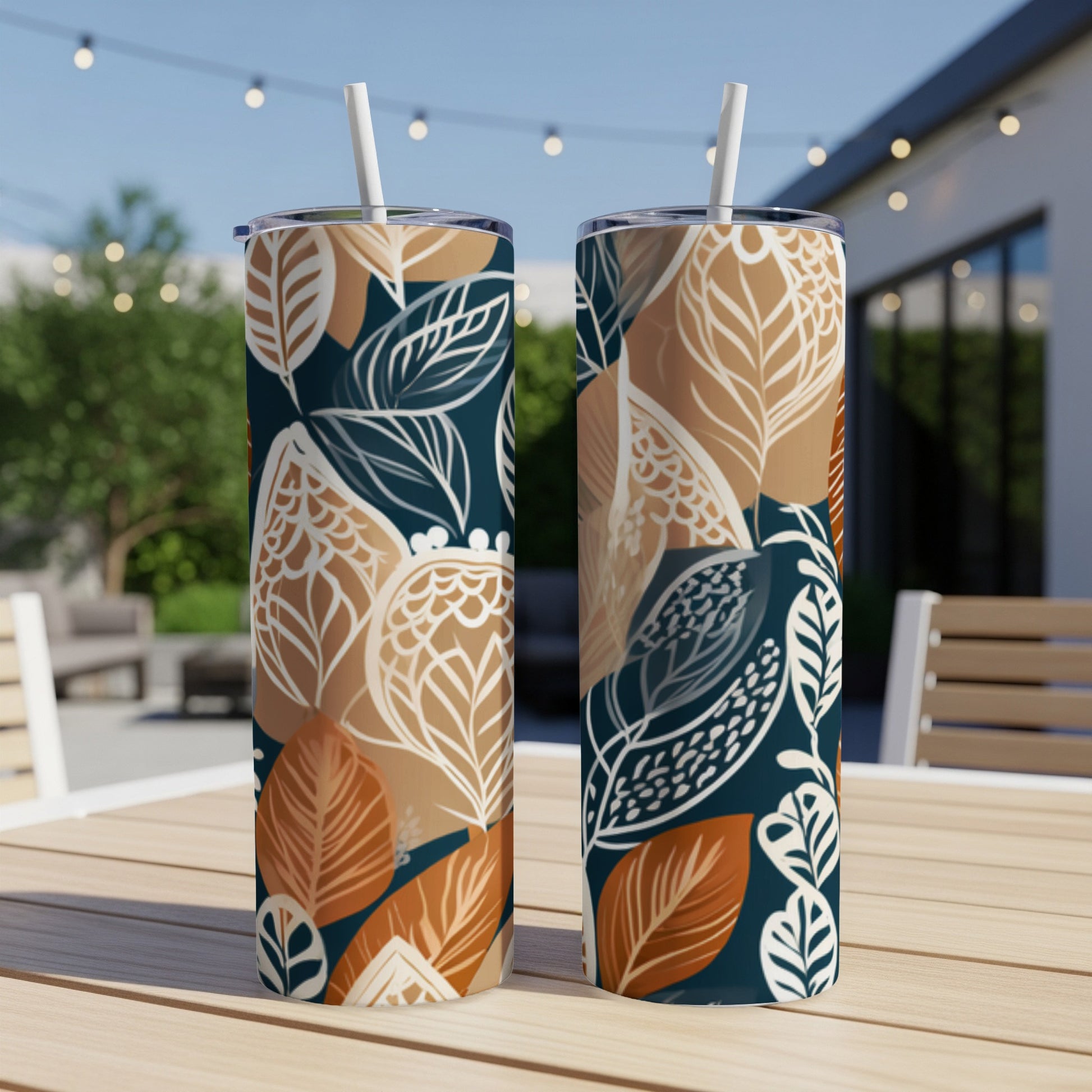 Two tumblers with a dark blue and tan leaf pattern, with straws.