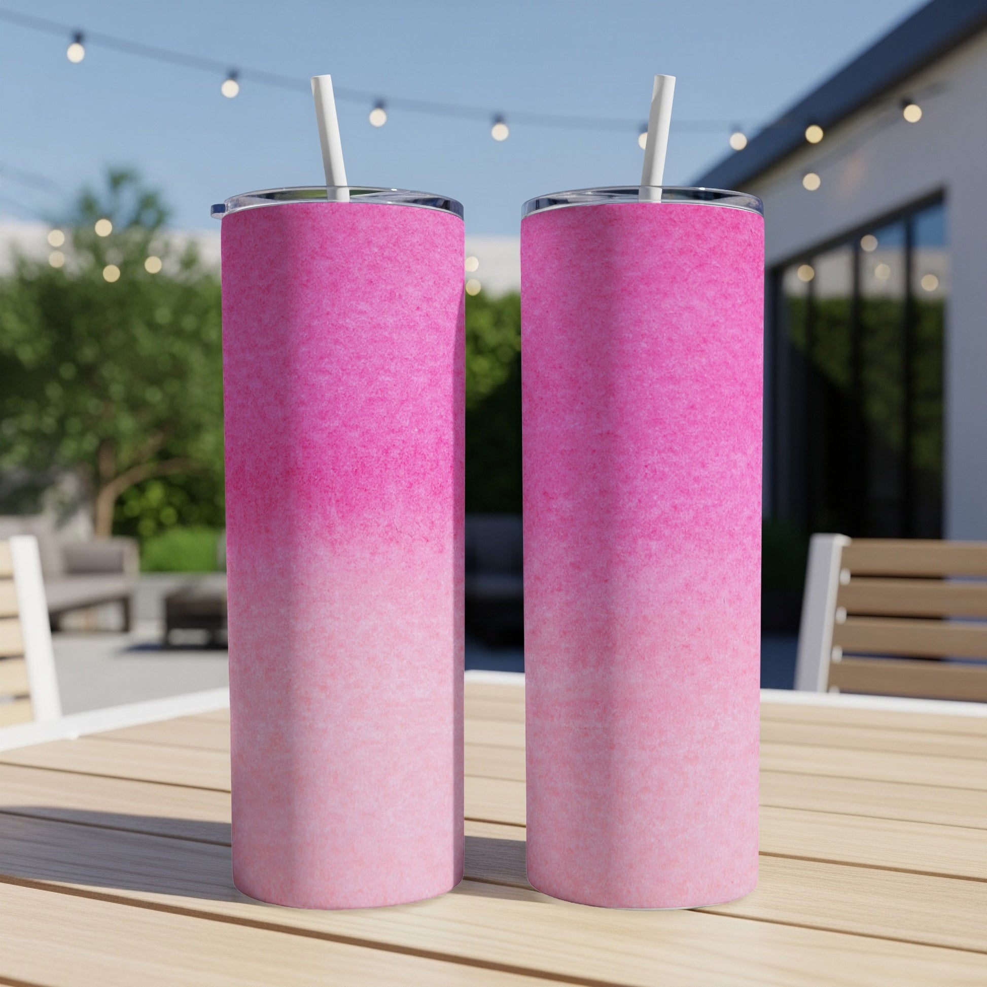 Two pink gradient tumblers with straws on a wooden table outdoors.