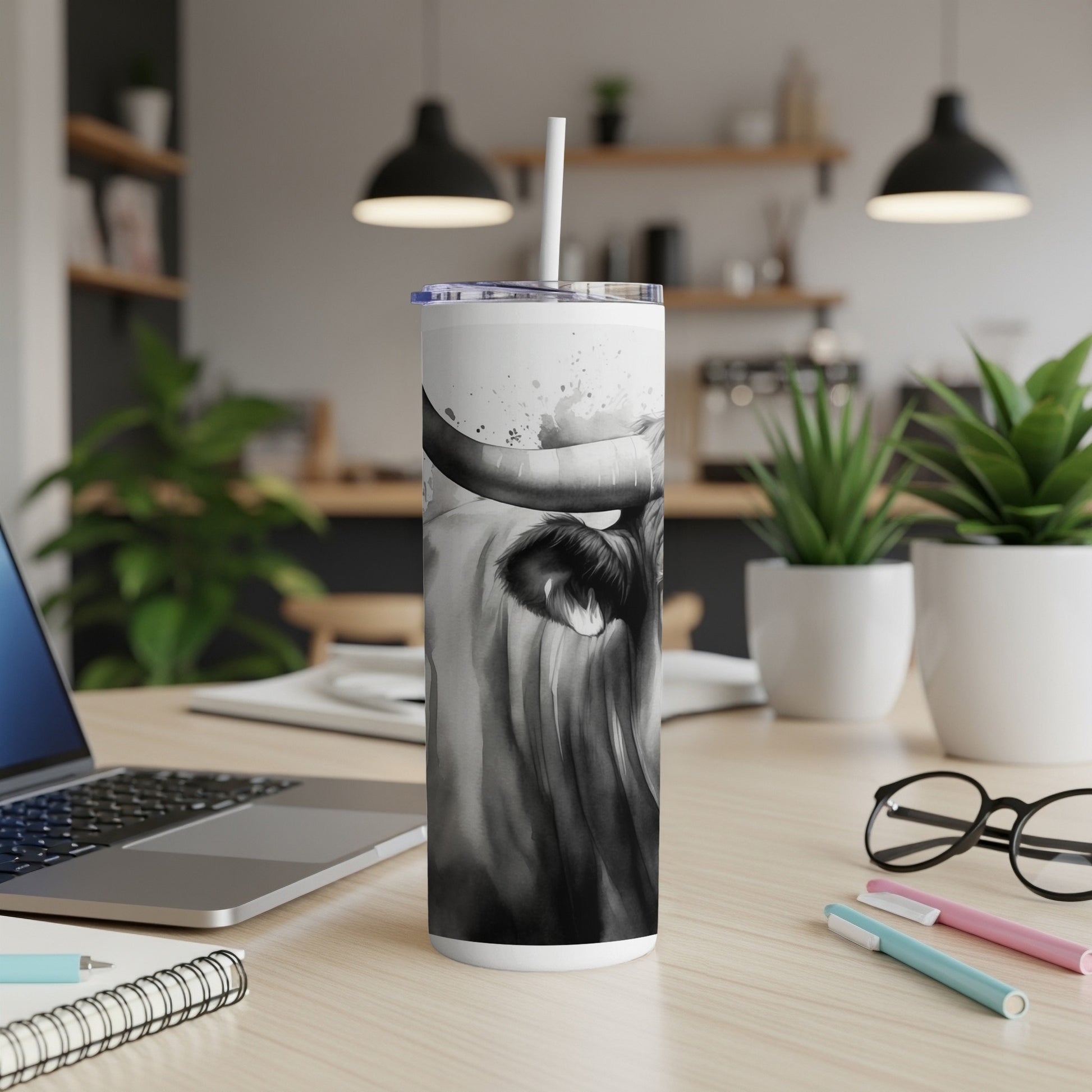 Black and white highland cow tumbler with straw on a desk.