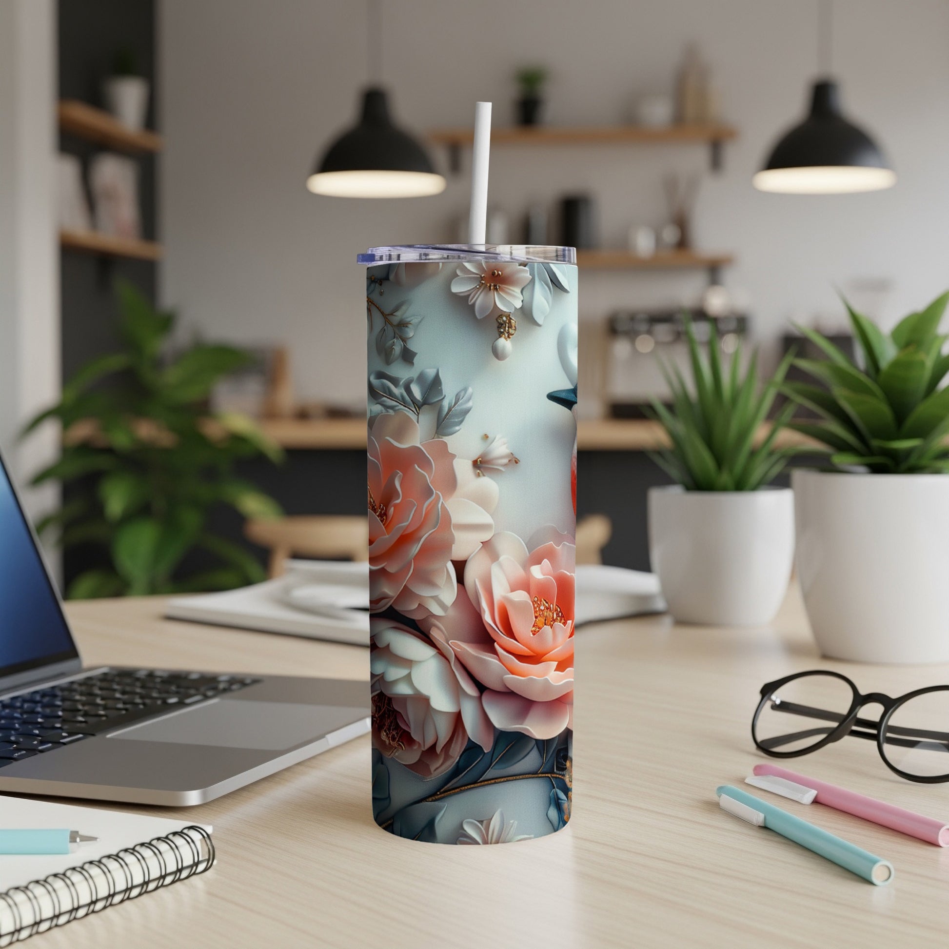 Floral tumbler with straw on a wooden desk with laptop and pens.
