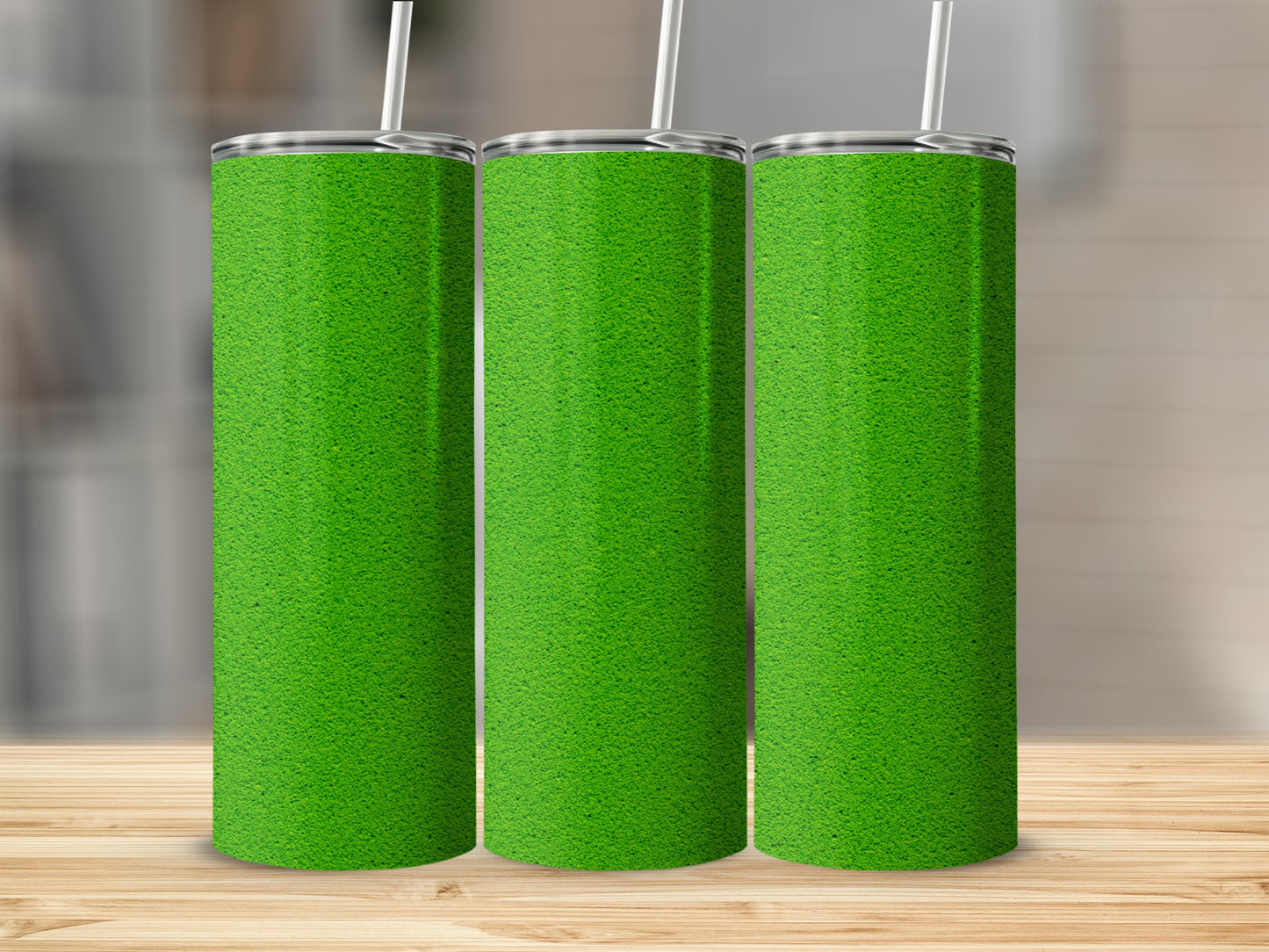 Three green grass-textured tumblers with straws stand on a wooden surface.