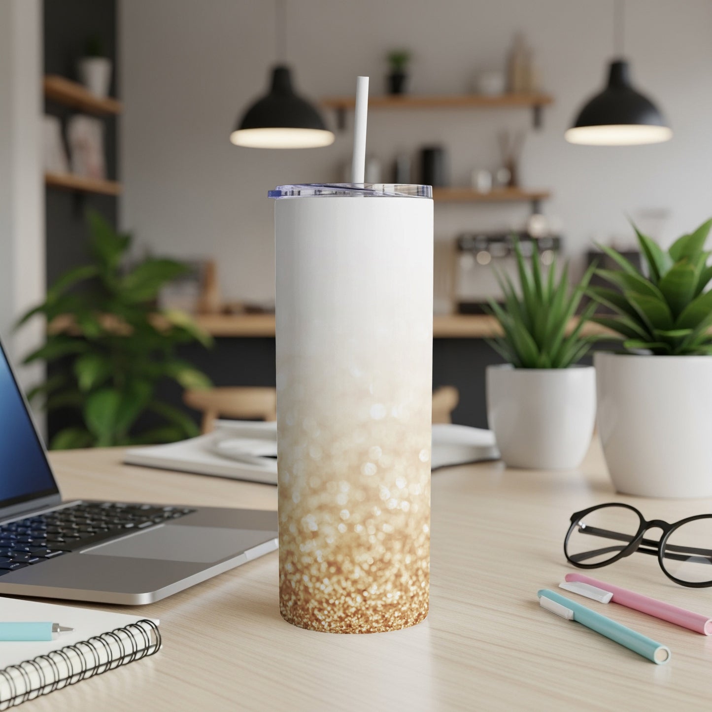White and gold glitter tumbler with straw on a wooden desk.