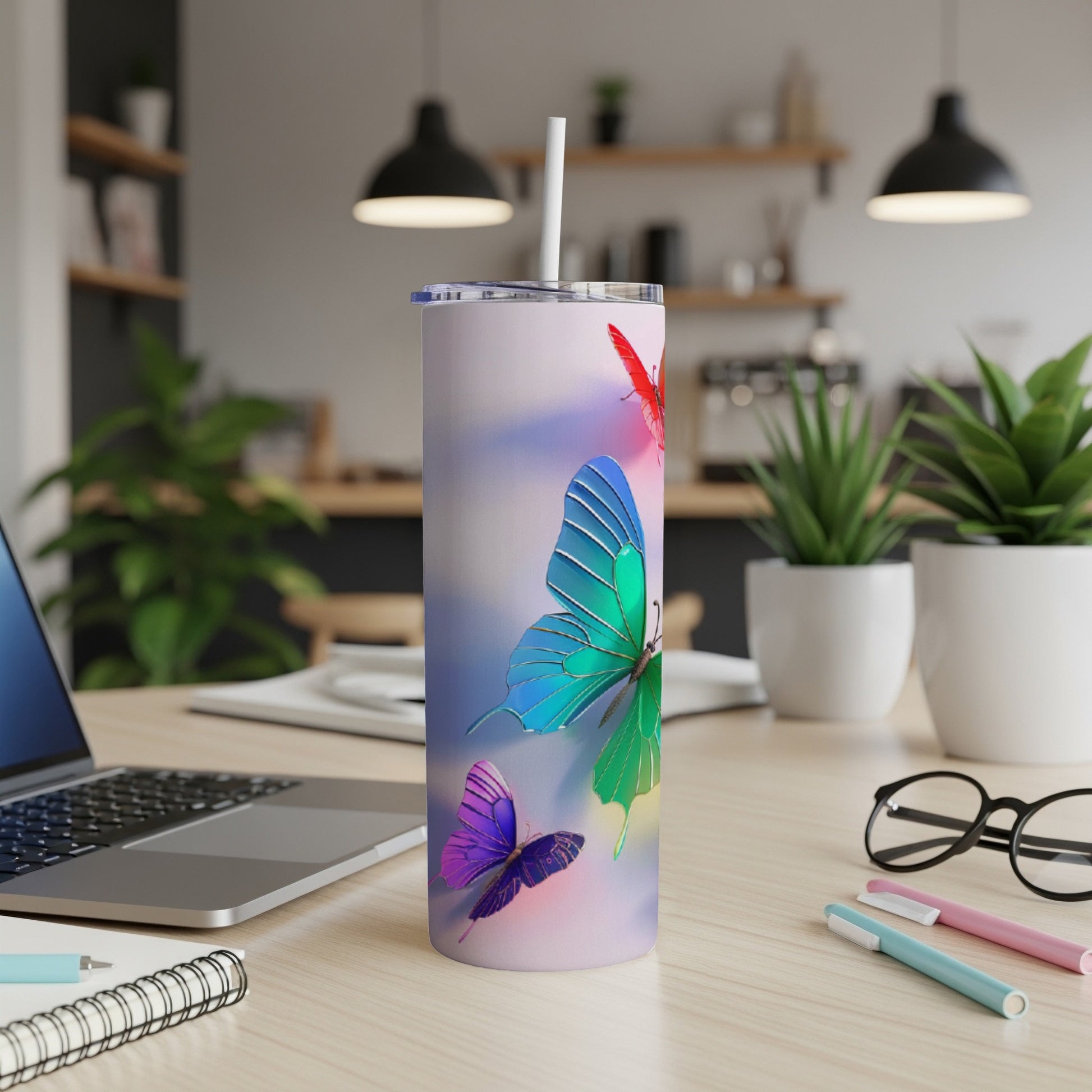 Tall, thin tumbler with colorful butterflies and a straw, on a desk.