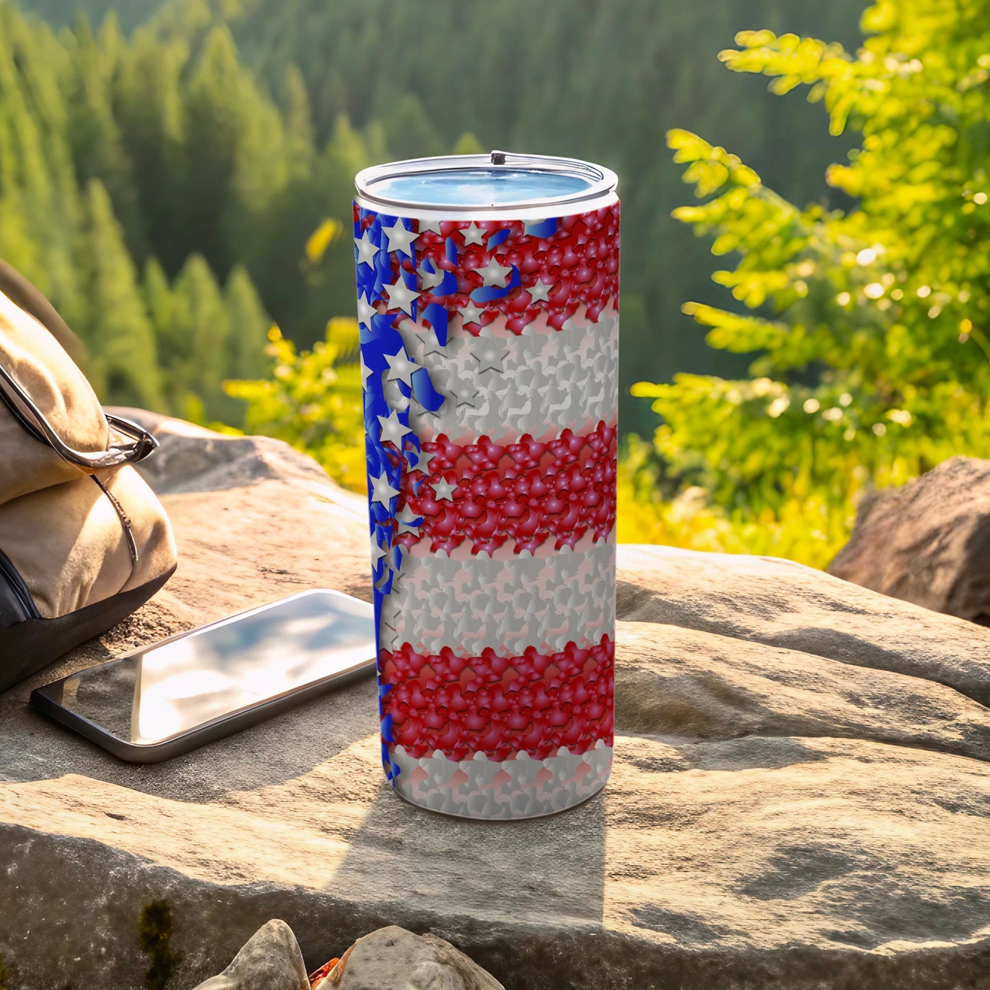 Tumbler with patriotic stars and stripes pattern on a rock with a phone and backpack.