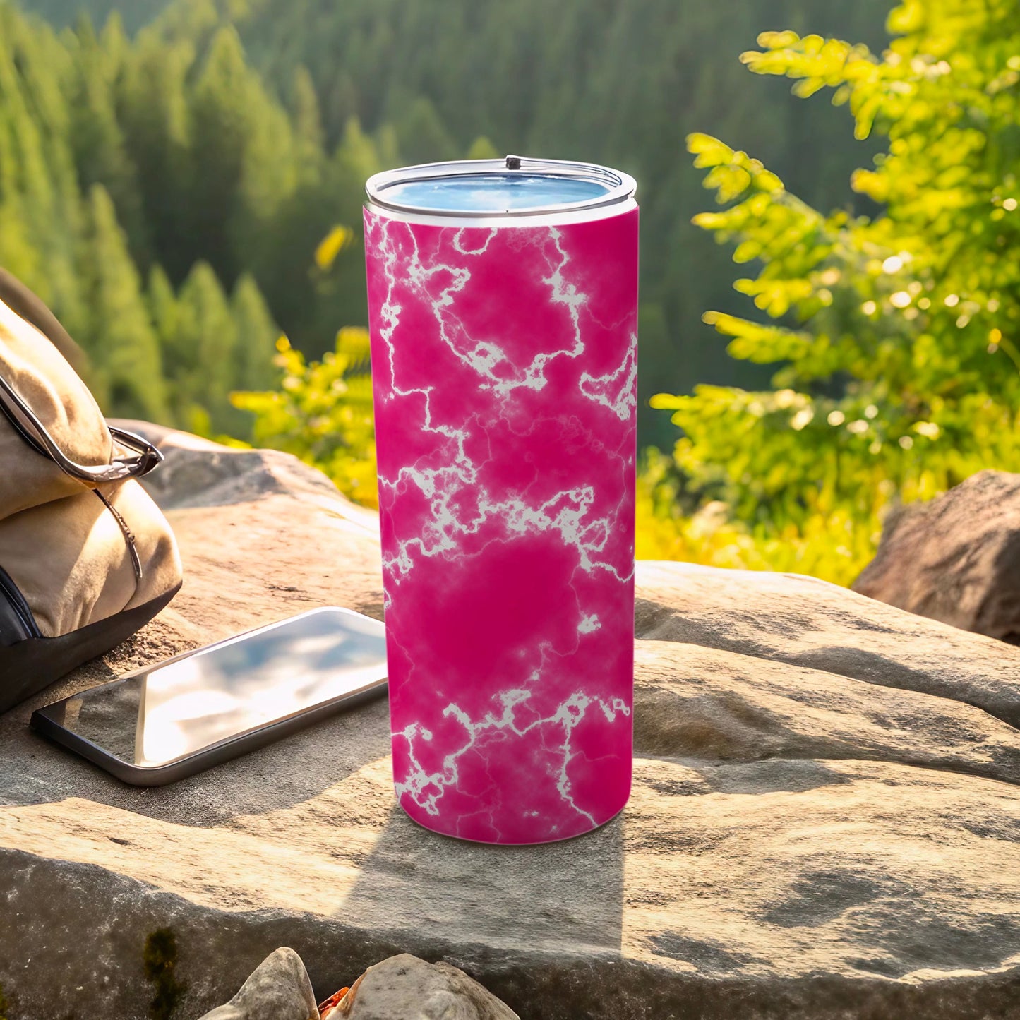 Pink marble tumbler on rocky surface with phone and backpack.
