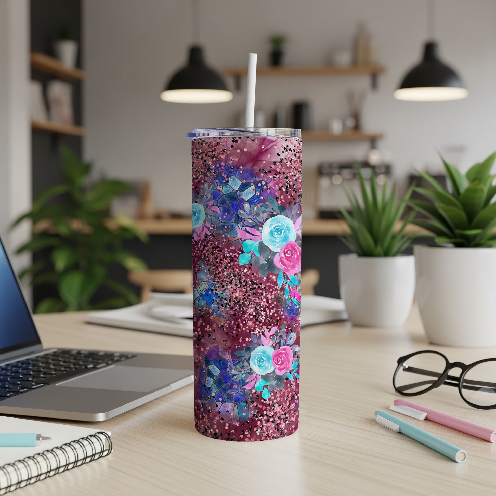 Tumbler with floral and glitter design on desk next to laptop and pens.