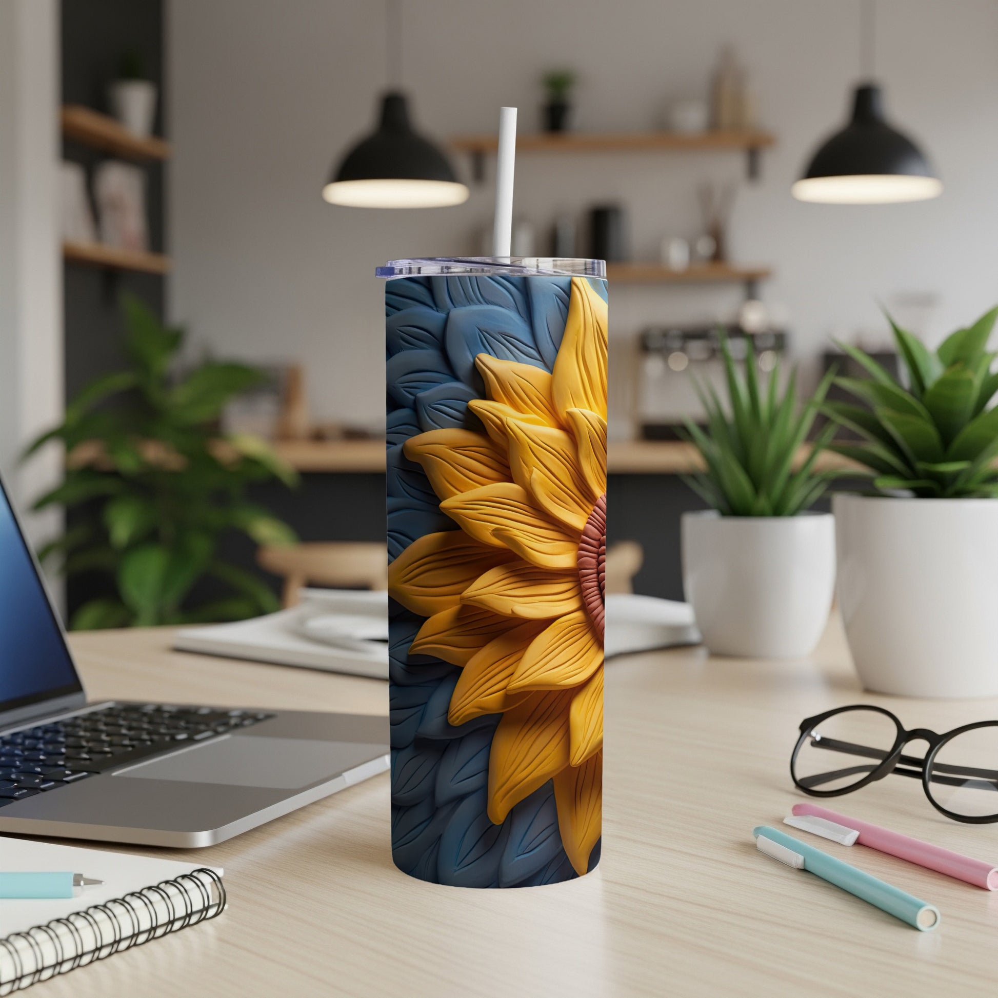 Yellow sunflower on a blue patterned tumbler with a straw on a desk.