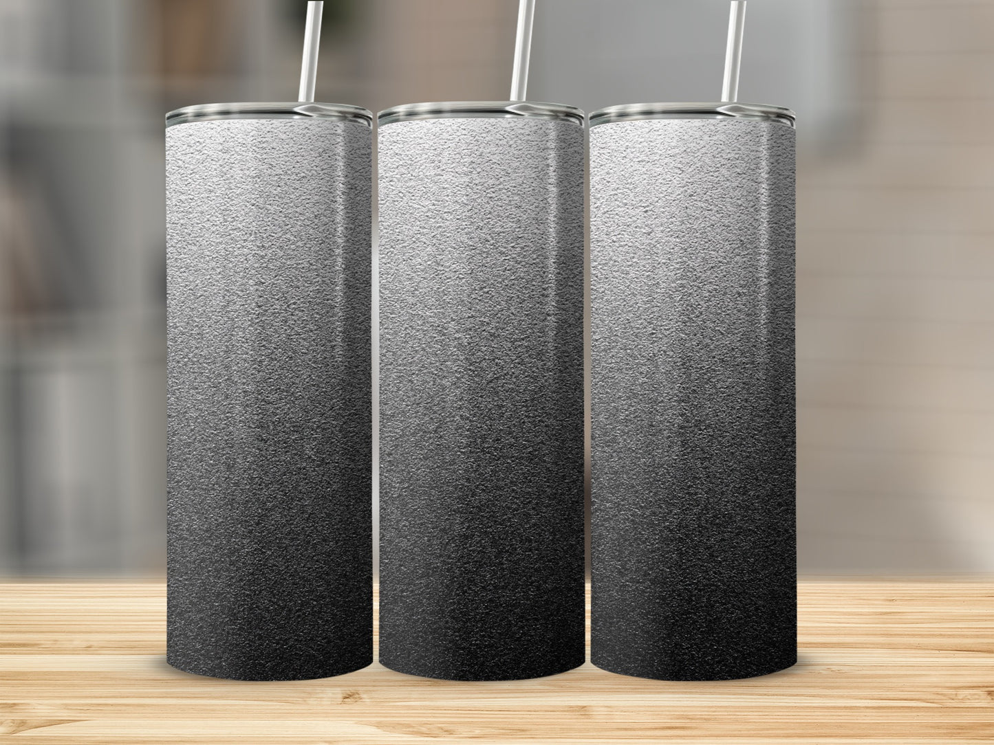 Three silver gradient tumblers with white straws on a wooden surface.