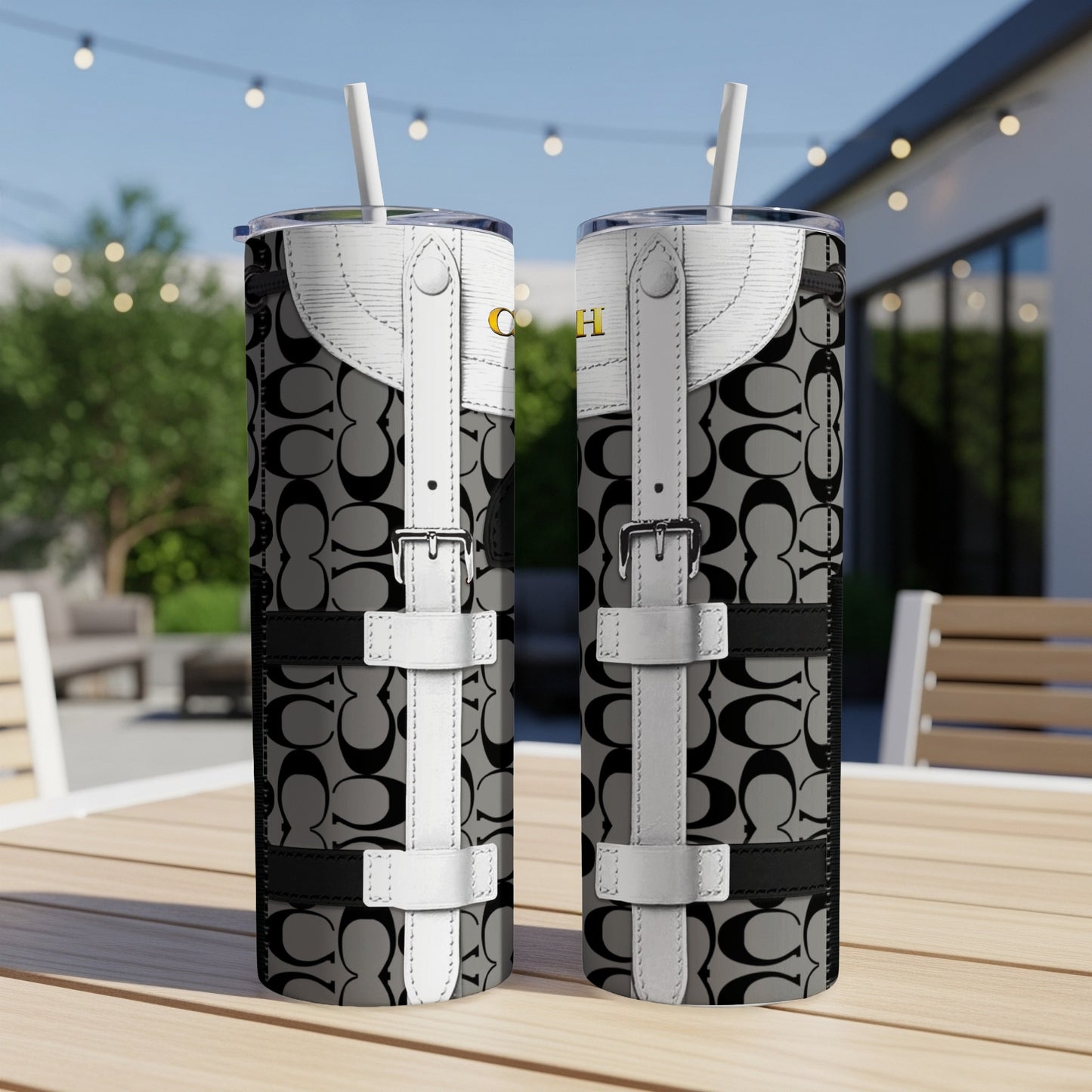 Two tumblers with Coach logo pattern and white buckle details sit on a table.