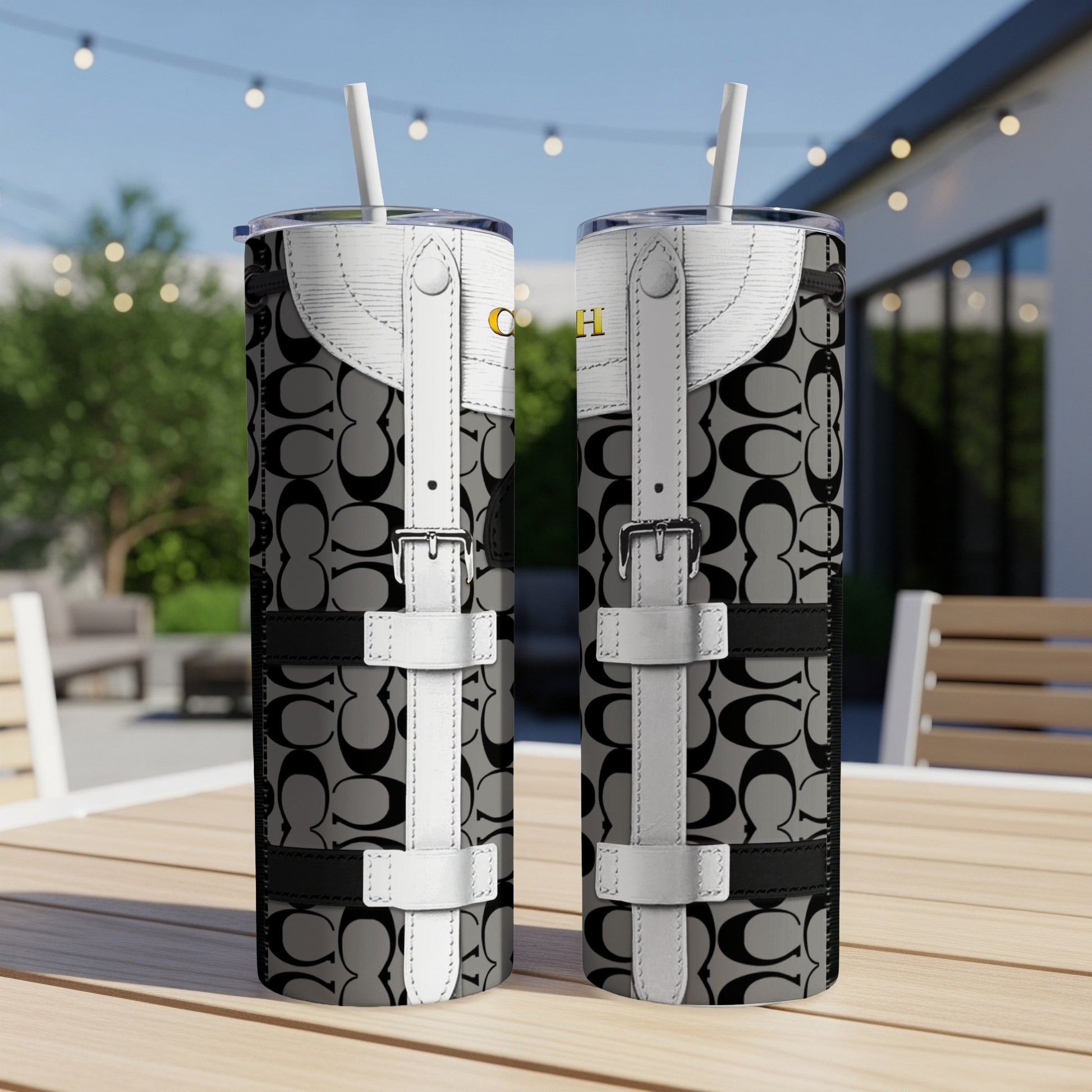 Two tumblers with Coach logo pattern and white buckle details sit on a table.