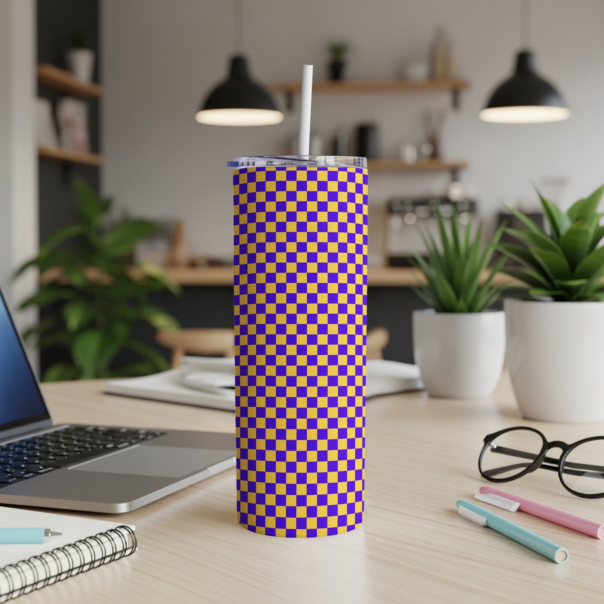 Purple and gold checkered tumbler with a white straw on a wooden desk.