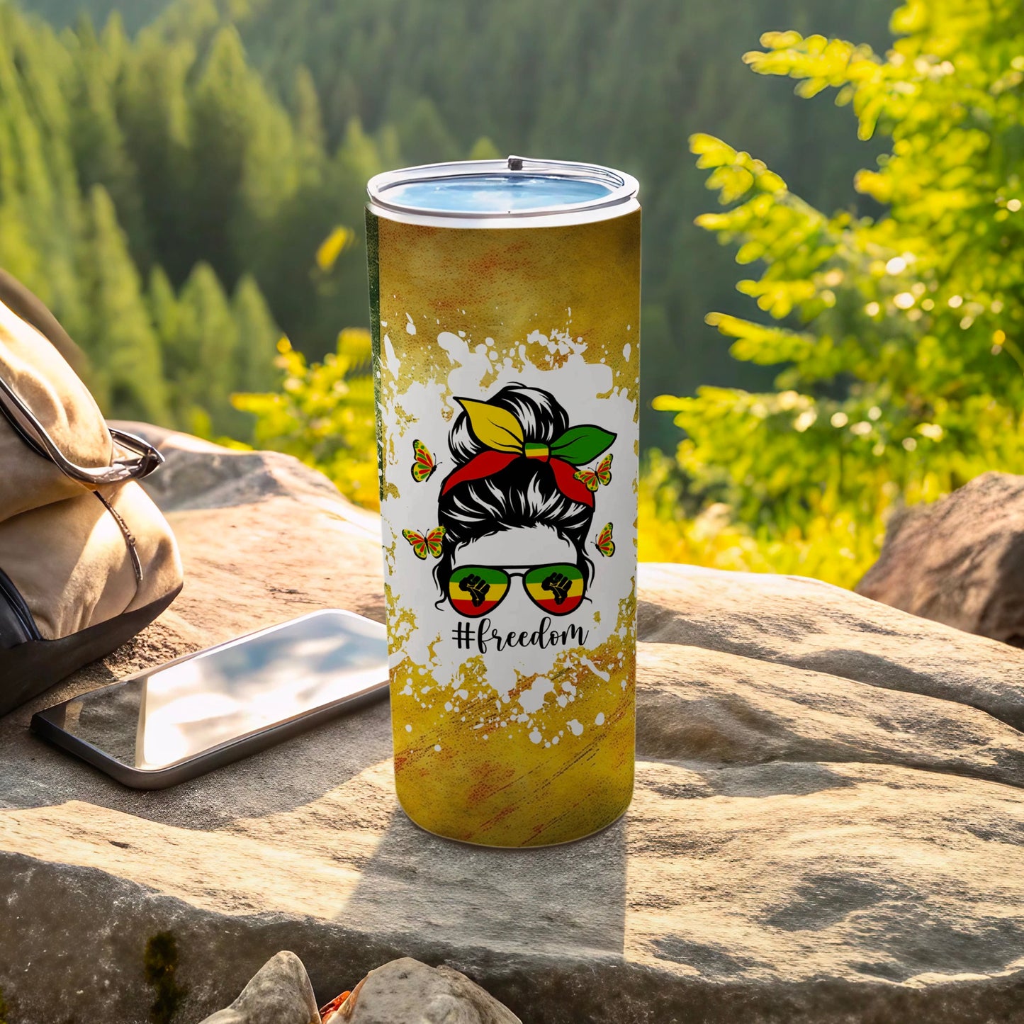 Tumbler with #Freedom, sunglasses, and butterflies design on a scenic rocky background.