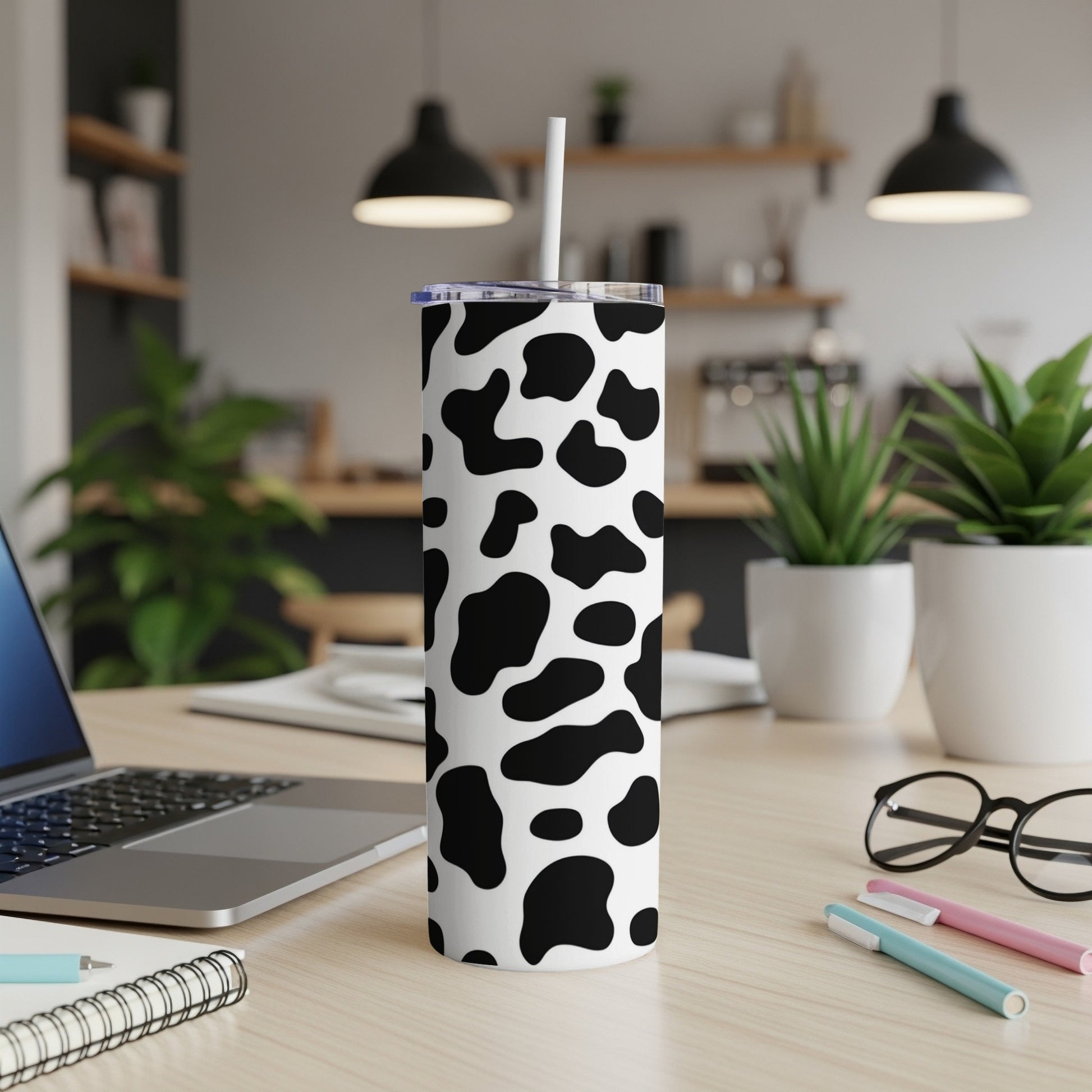 Black and white cow print tumbler with straw on a desk.