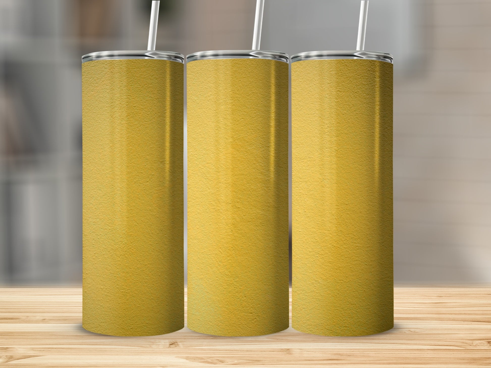Three gold textured tumblers with white straws stand on a wooden surface.