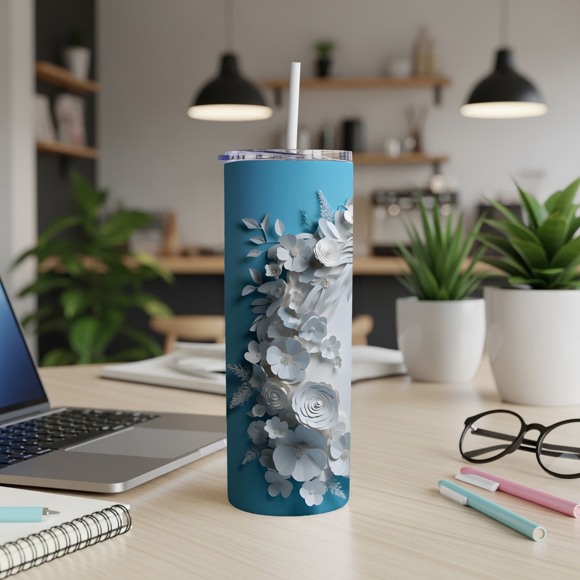 Blue tumbler with white floral design on desk with laptop and pens.
