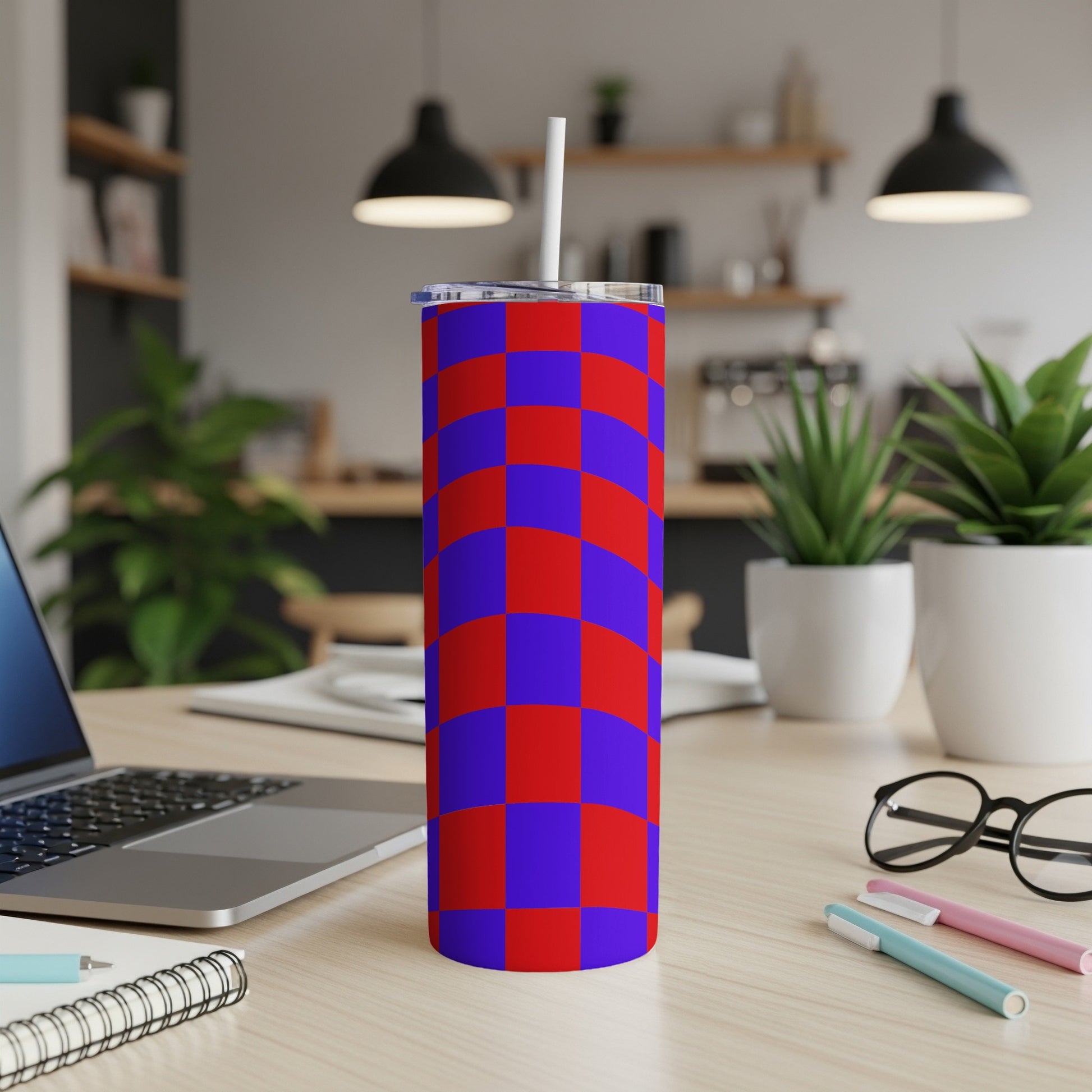 Red and blue checkerboard pattern tumbler with straw on a desk.