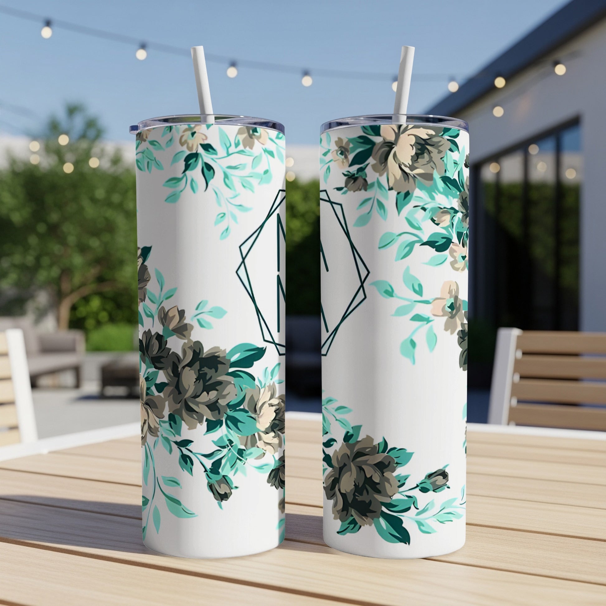Two white tumblers with floral patterns and a geometric monogram sit on a table.