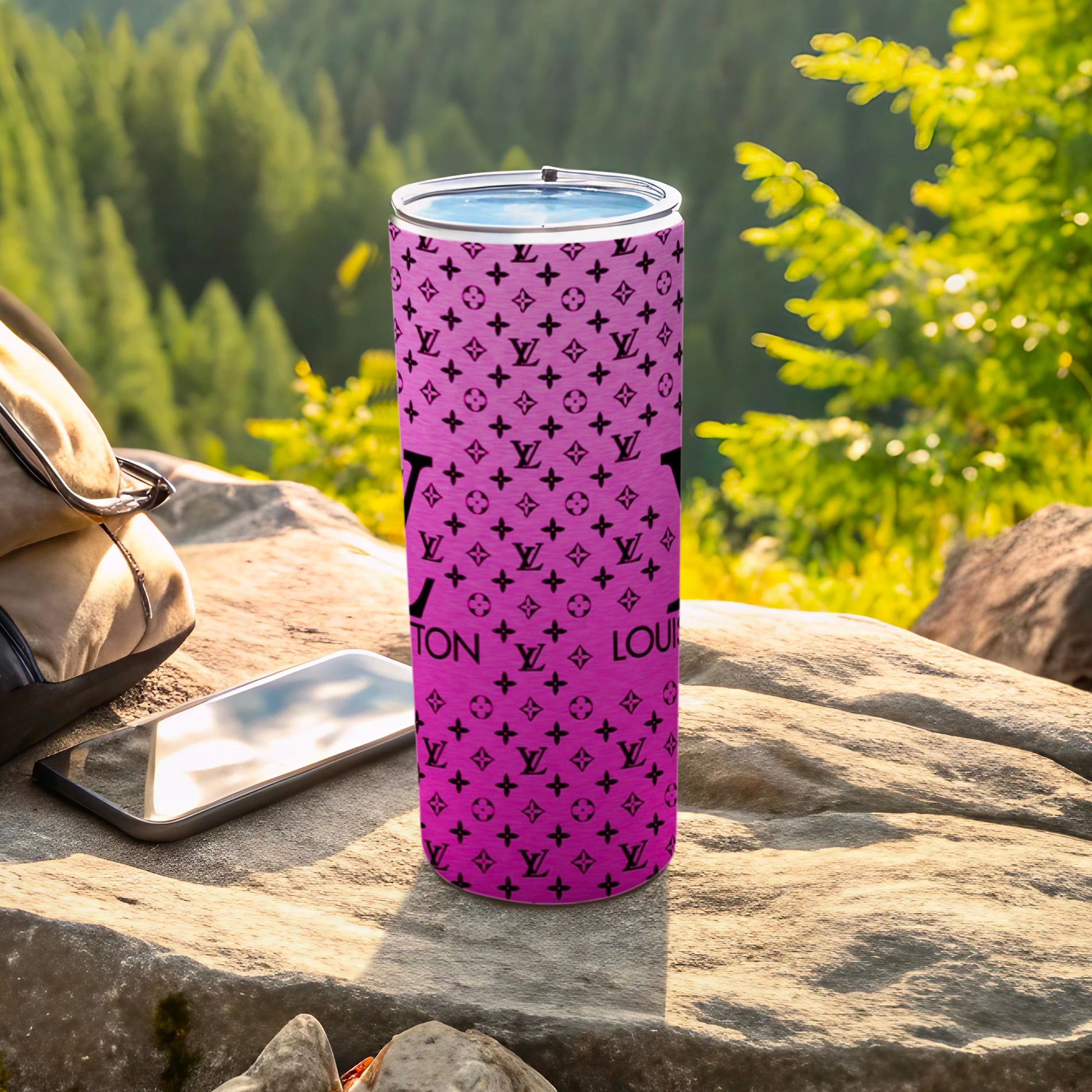 Pink tumbler with Louis Vuitton monogram pattern on outdoor rock surface.