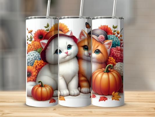 Two kittens, one white and one orange, sit with pumpkins and flowers.