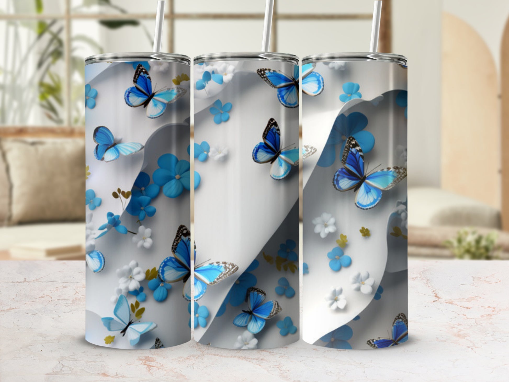 Three tumblers with blue butterflies and white flowers on a marble surface.