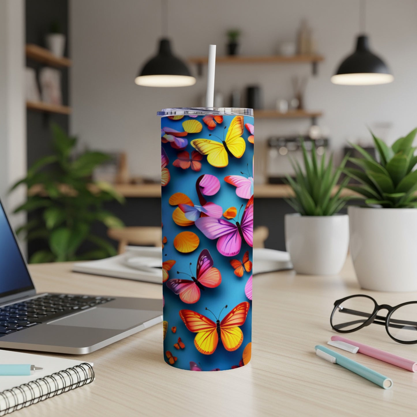 Tall tumbler with colorful butterflies and circles, on a desk with laptop and pens.