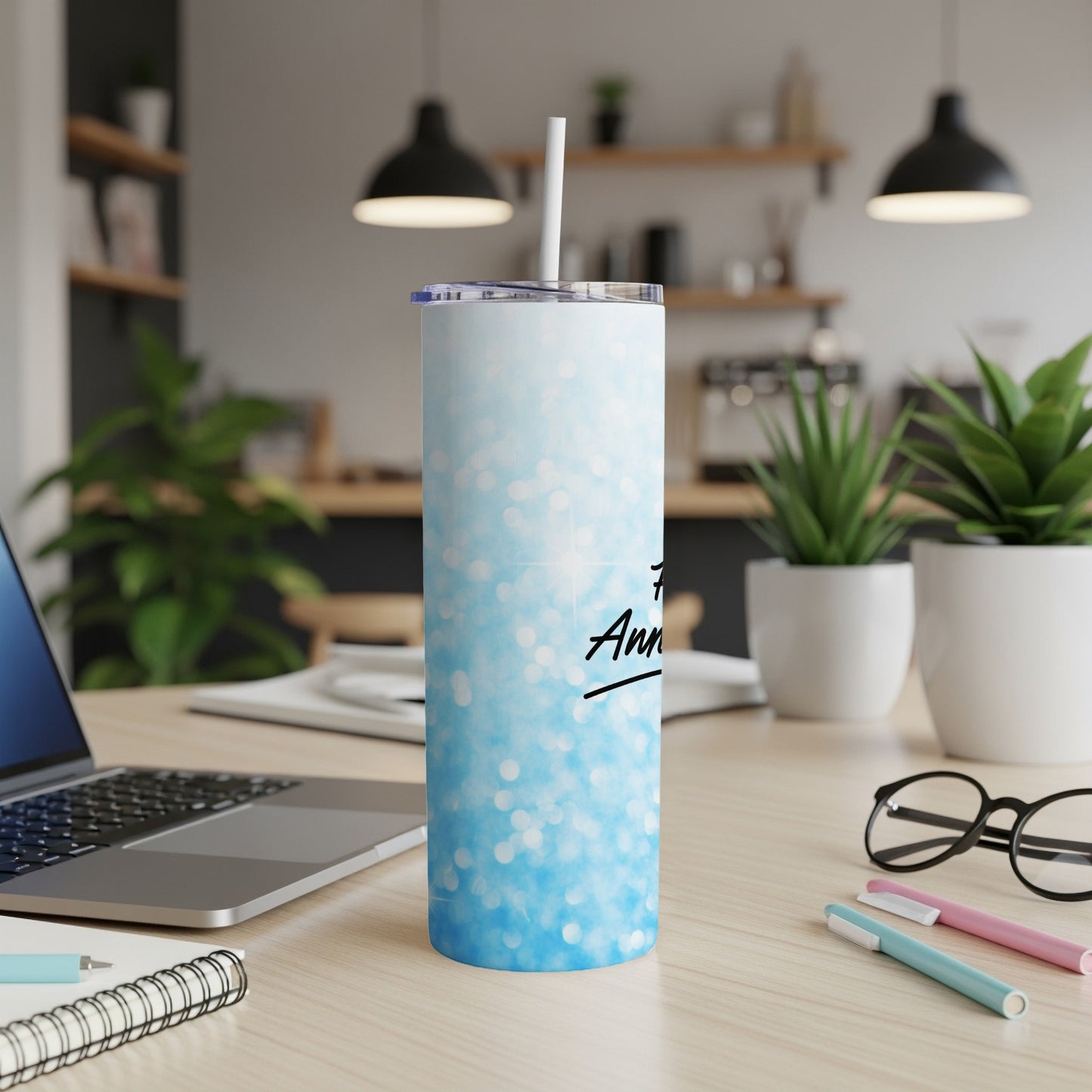 Blue glitter tumbler with "Anniversary" text and straw, on a desk.