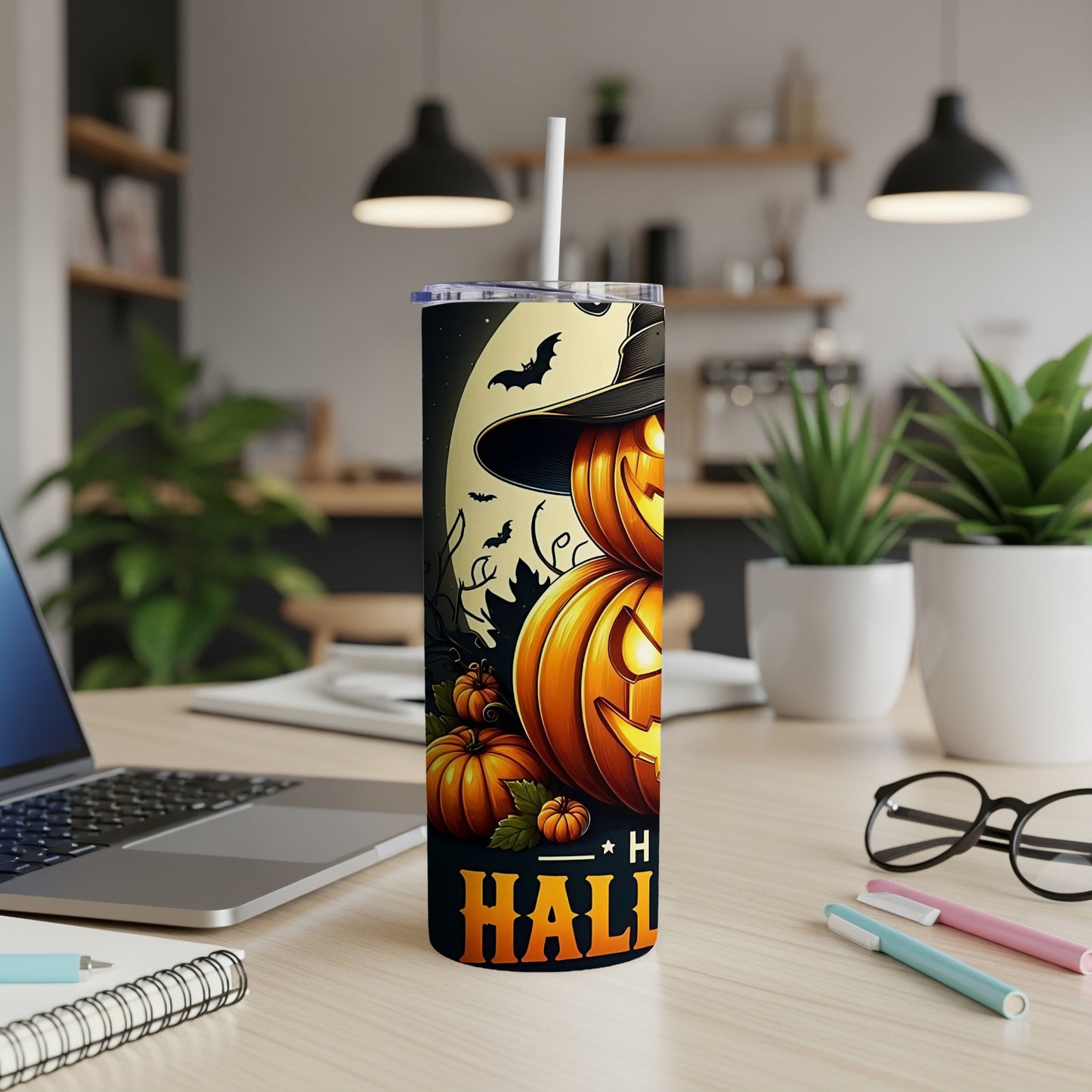 Halloween tumbler with pumpkins, bats, and a witch hat on a desk.