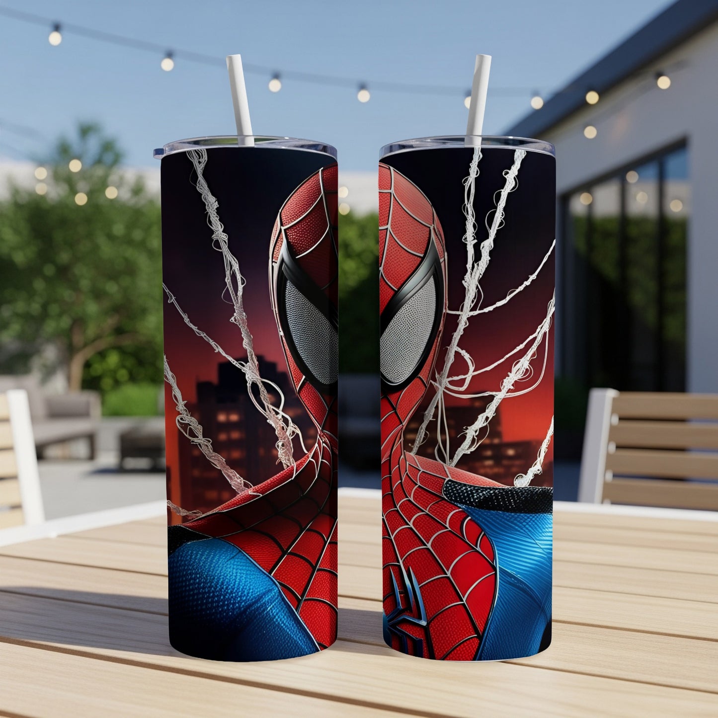 Two Spiderman-themed tumblers with straw on a table, city lights in background.
