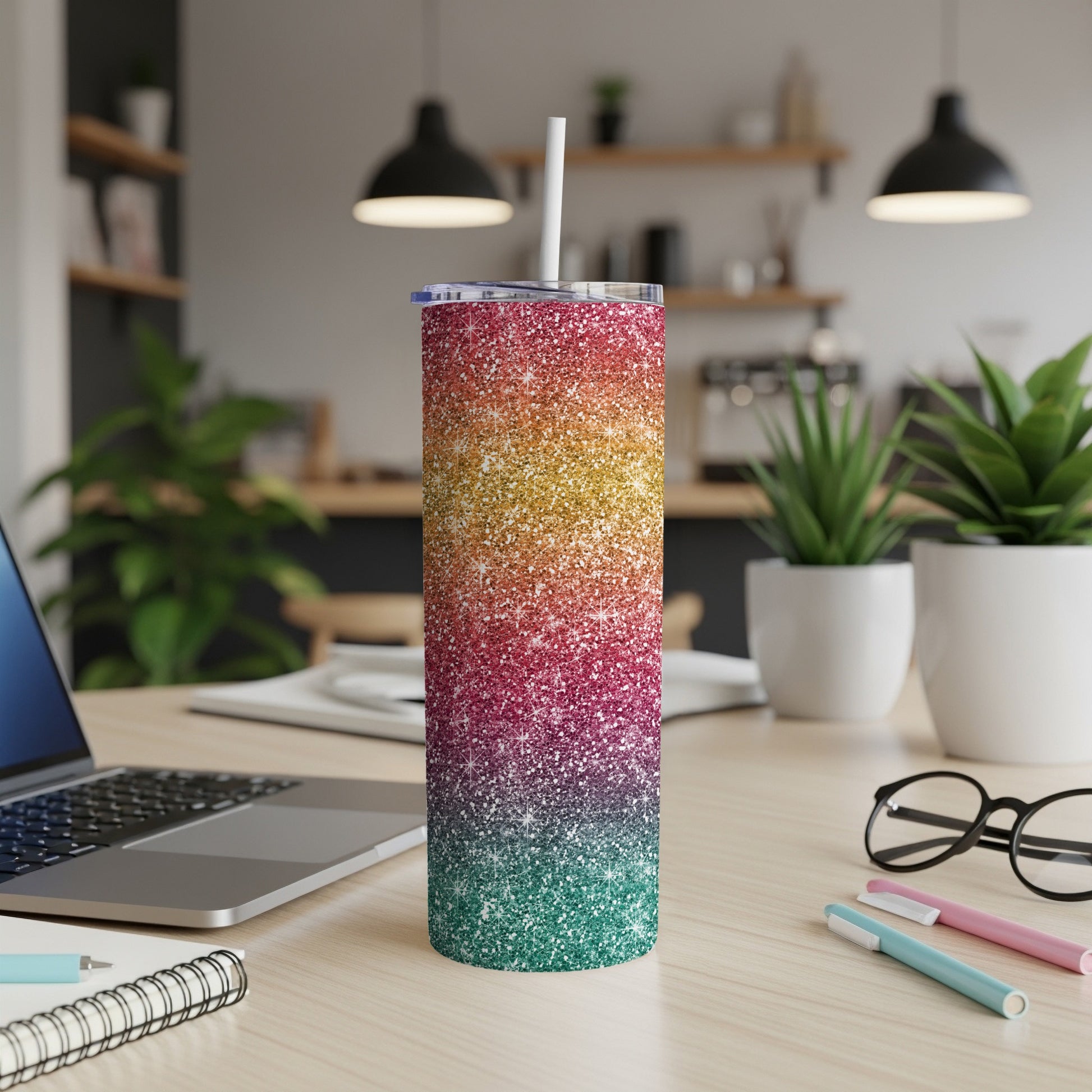 Glitter gradient tumbler with straw on a wooden desk with laptop and notebooks.