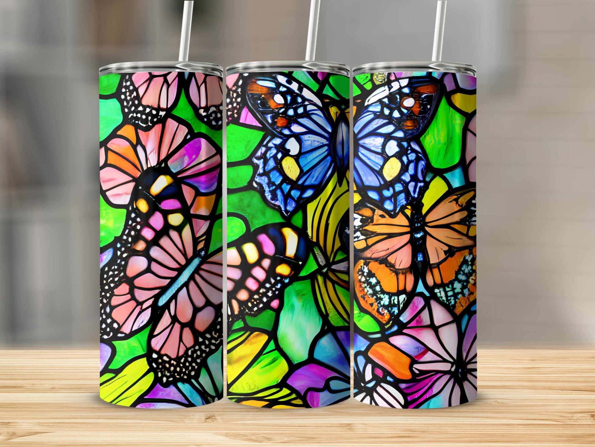 Three tumblers with stained glass butterfly designs on a wooden surface.