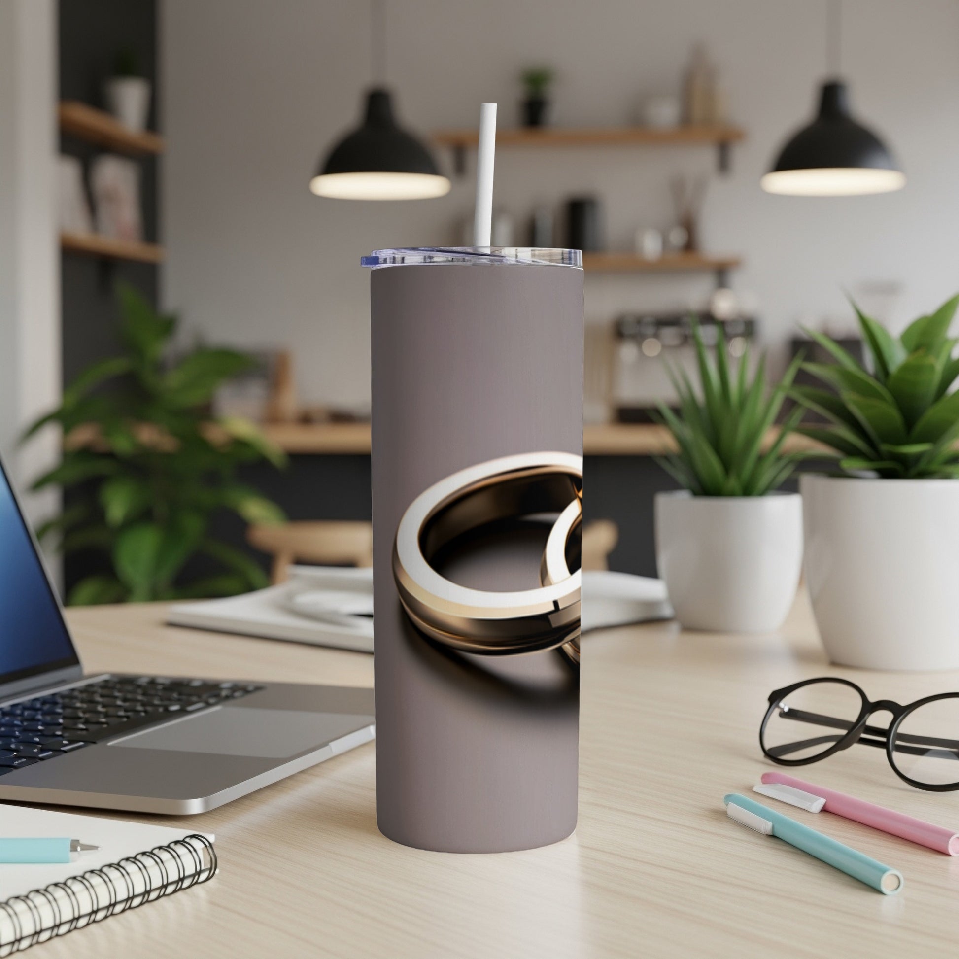 Gray tumbler with gold rings design and straw on a desk.