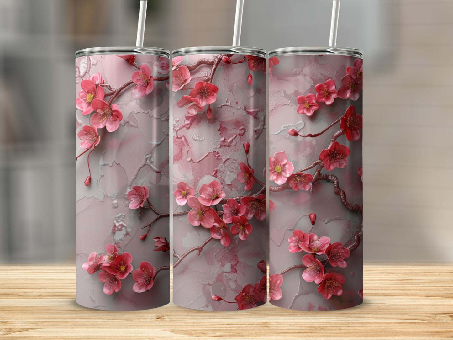 Three pink cherry blossom tumblers with straws on a wooden surface.