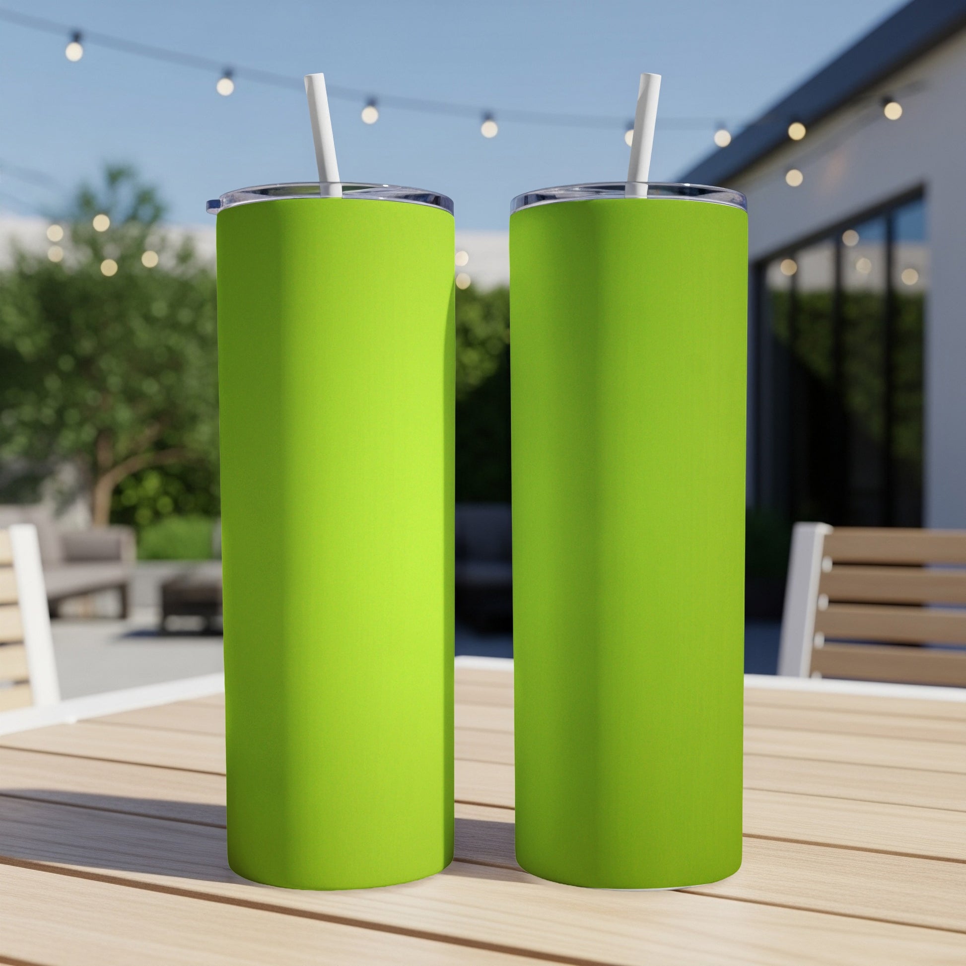 Two tall, lime green tumblers with straws on a wooden table outdoors.