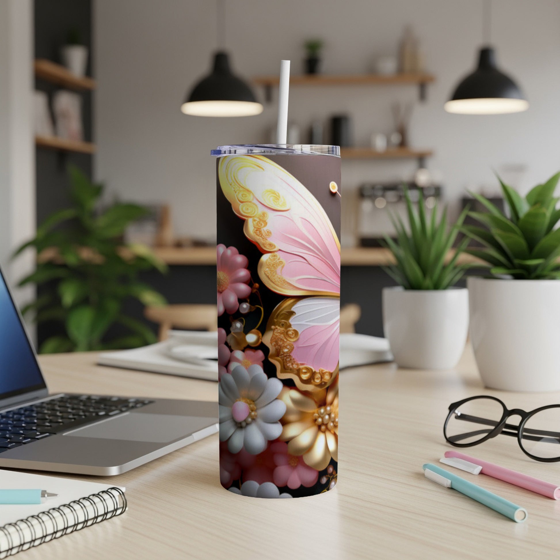 Brown tumbler with butterfly and floral design, on a desk with laptop and pens.